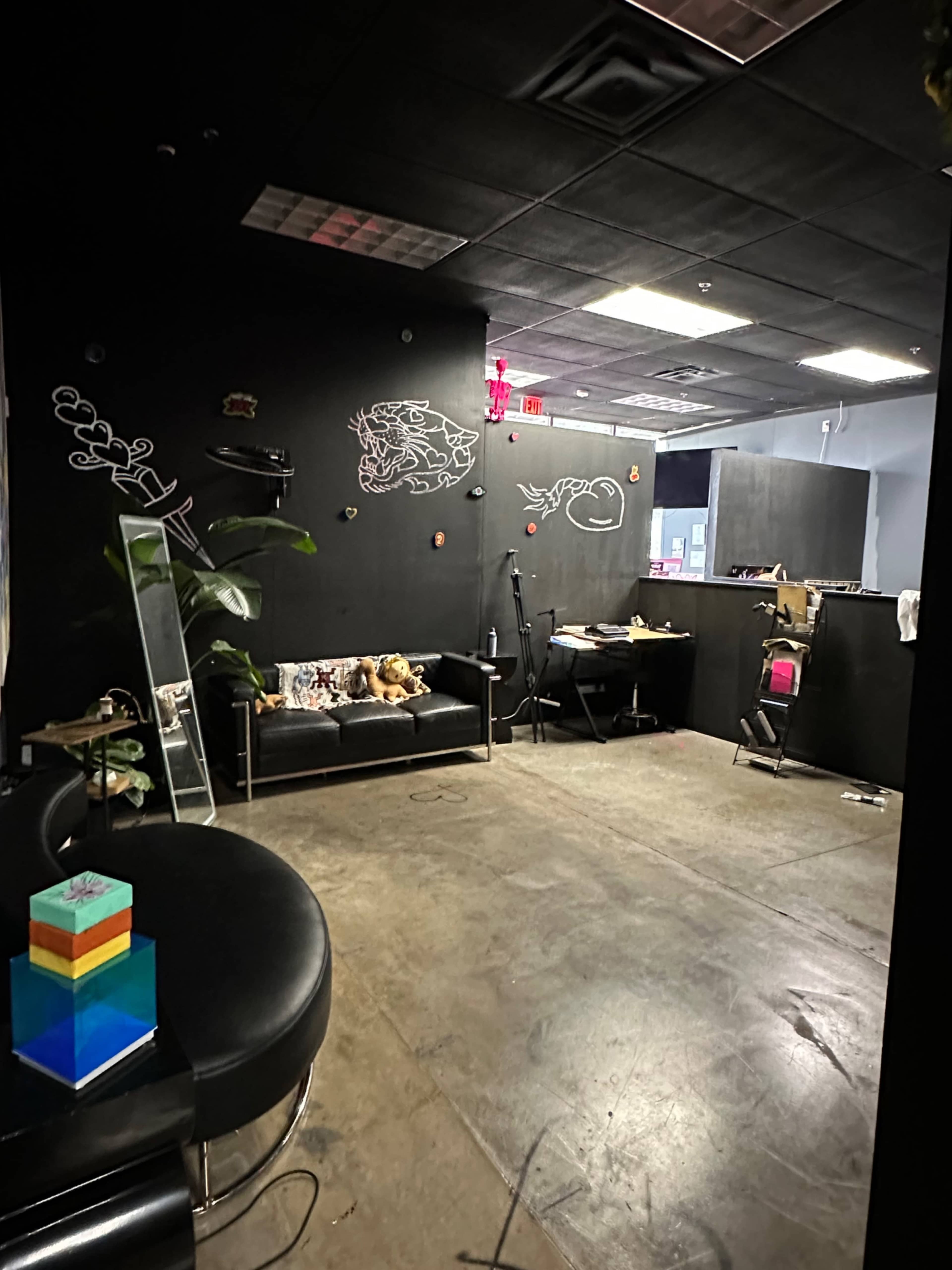 The image shows a sparsely furnished room with a black wall featuring graffiti, a couch with stuffed animals, a mirror, and a colorful stack of blocks on a curved black piece of furniture.