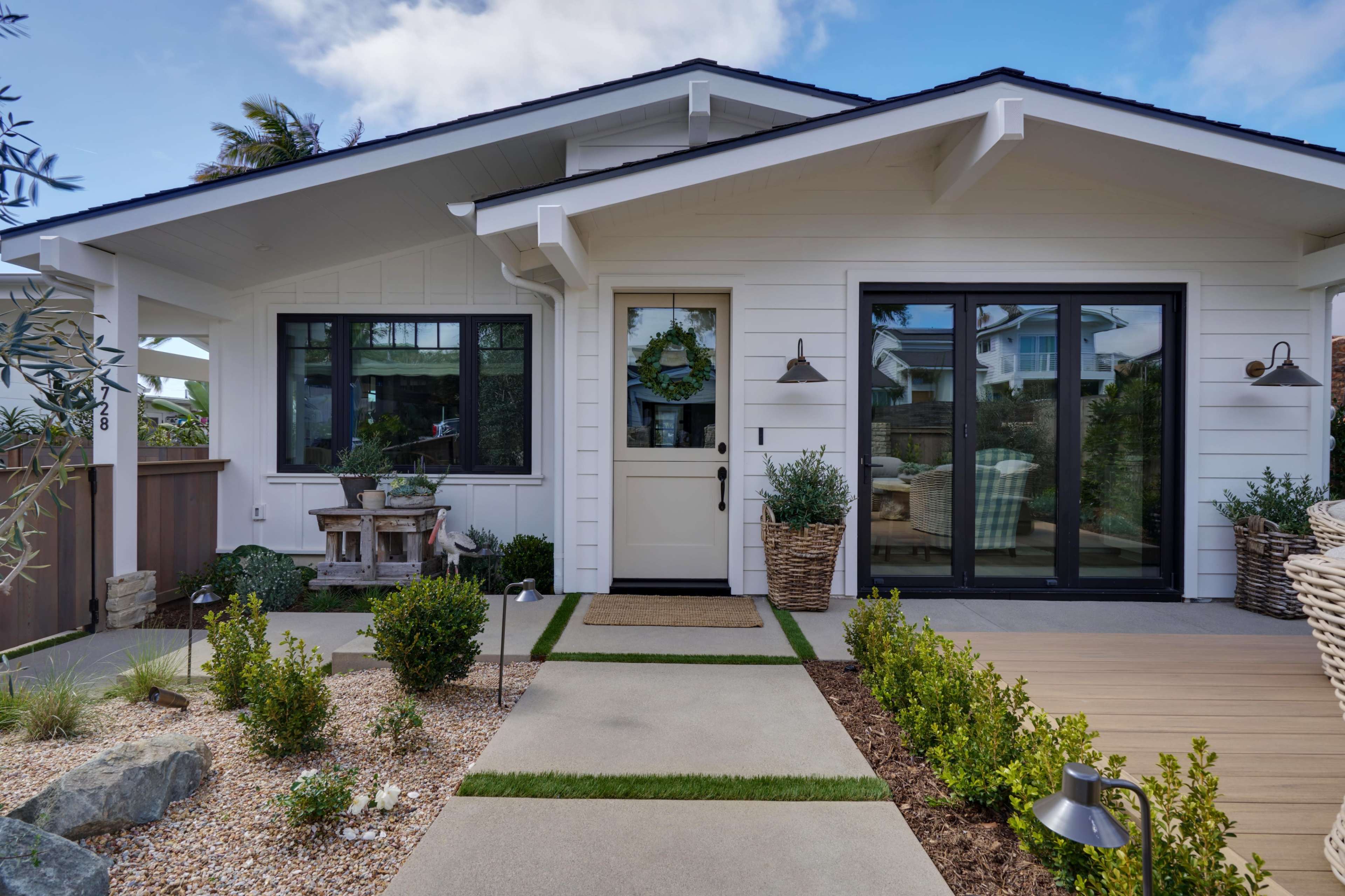 A modern single-story house with a white exterior, a welcoming front porch, and well-maintained landscaping featuring plants and stone pathways.