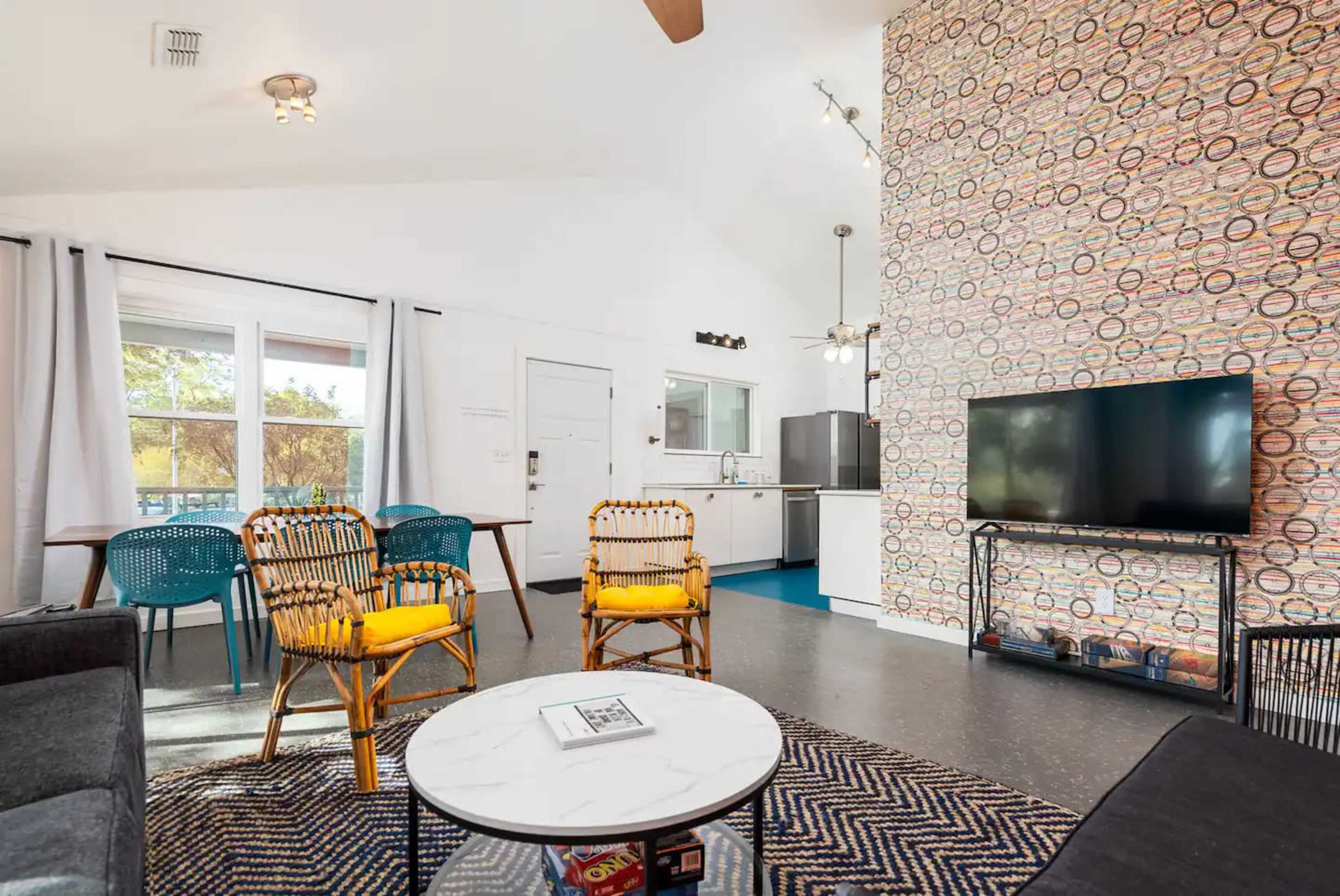 The living area features comfortable seating, a television, and a kitchen visible in the background with colorful decor on one wall.