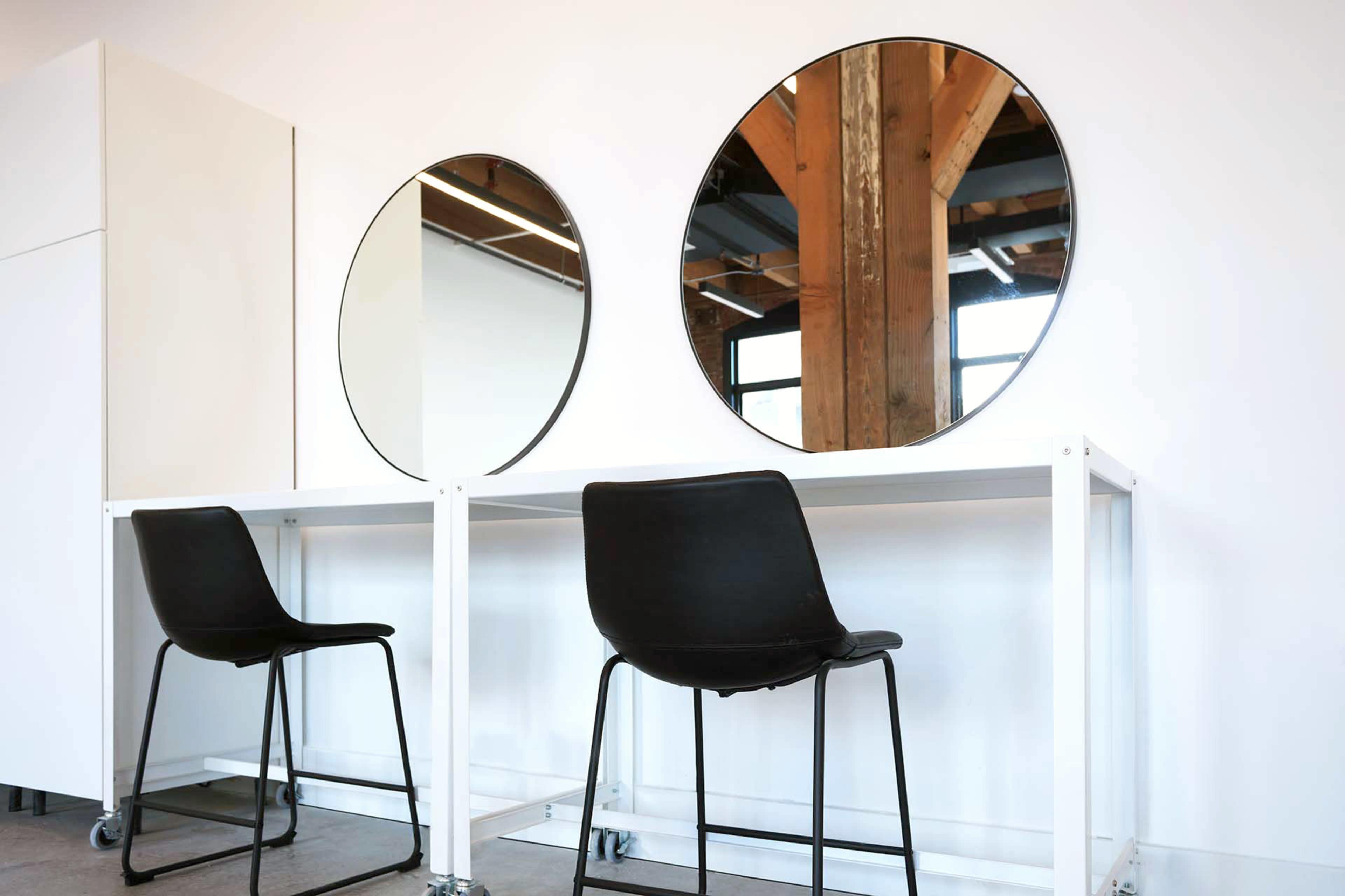 The image shows two circular mirrors mounted on a white wall above a minimalist white table with two black chairs.