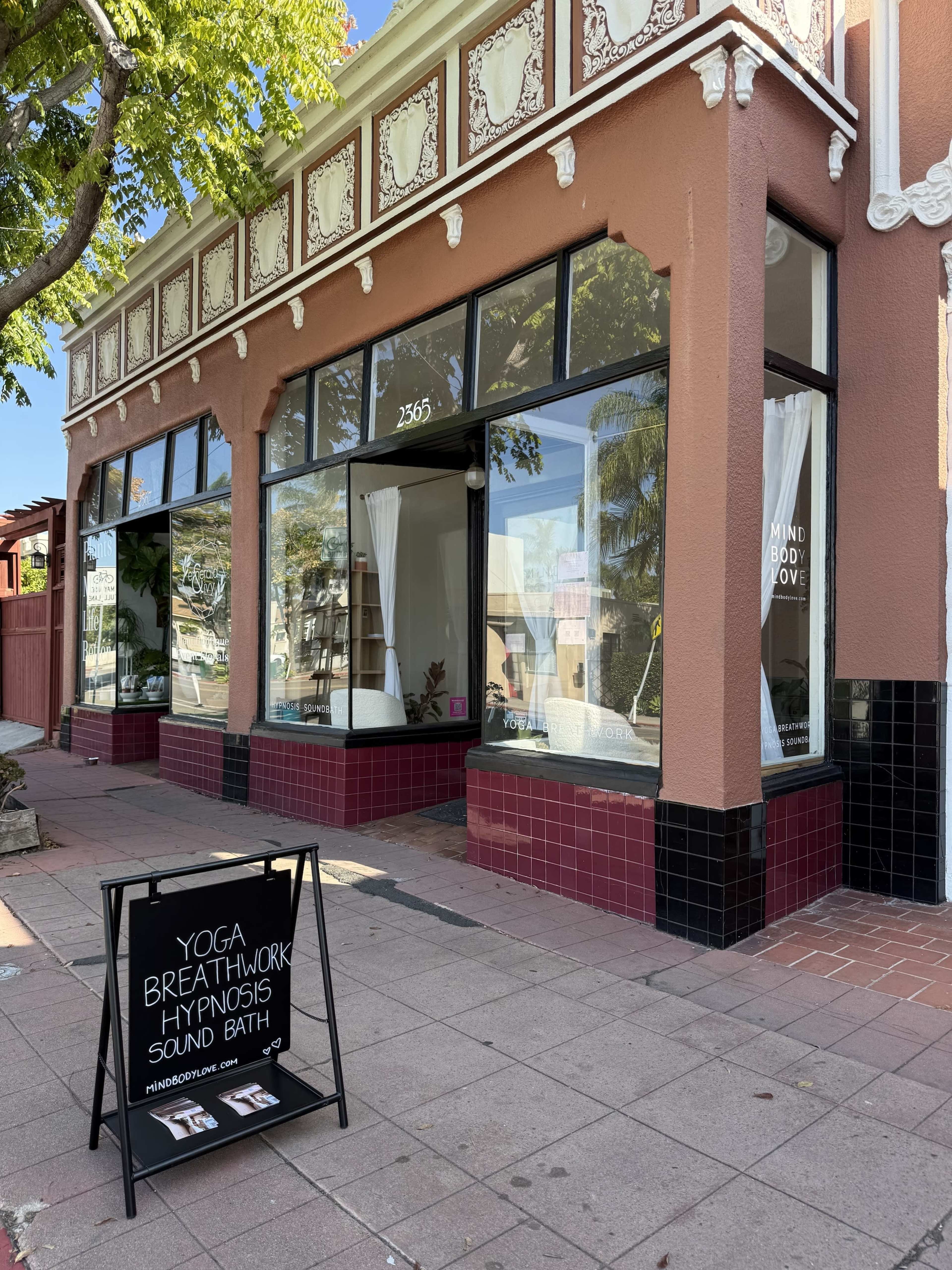 The image shows a wellness studio storefront with large windows displaying a sign that offers yoga, breathwork, hypnosis, and sound bath sessions.