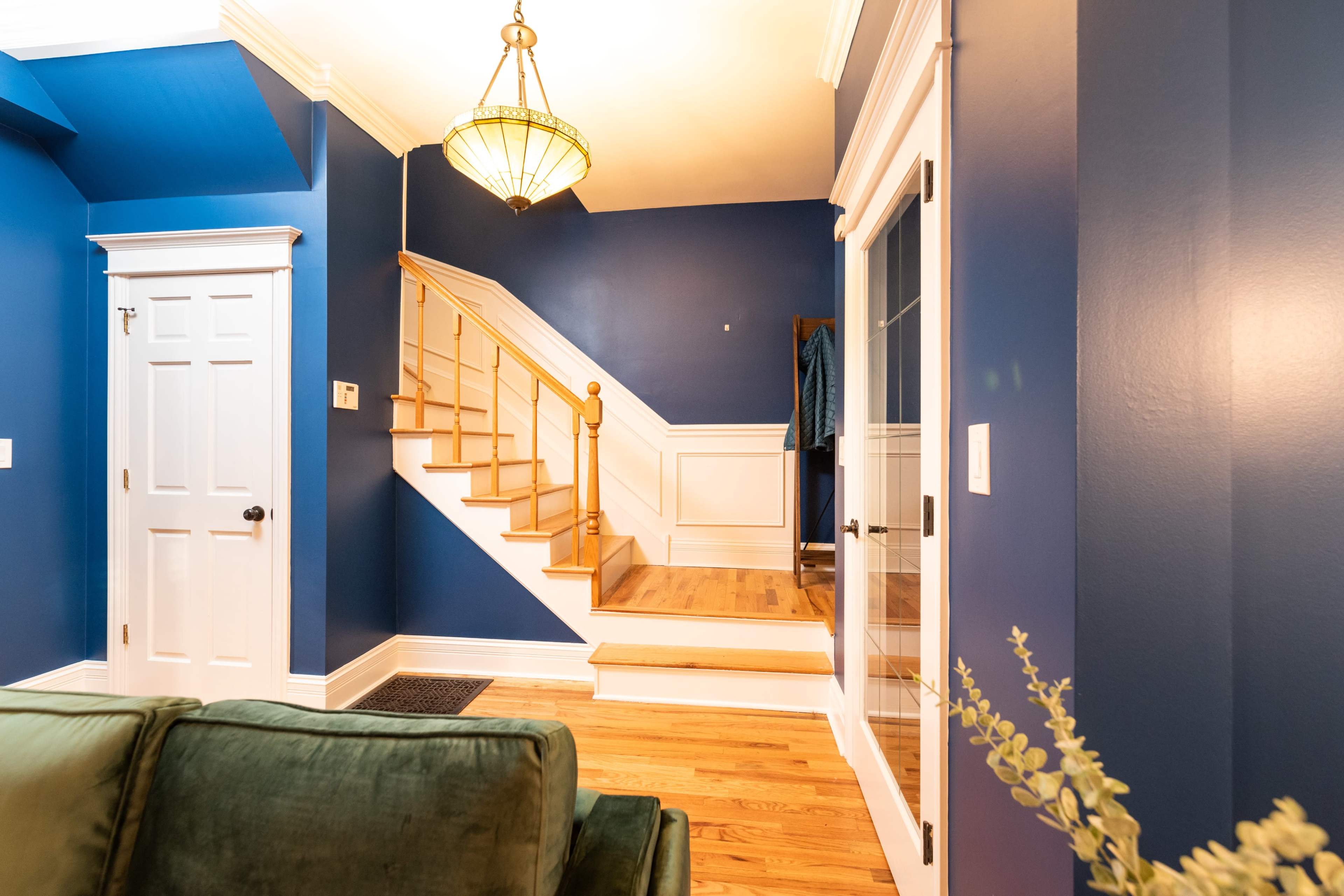 The image shows a blue-walled entryway with a staircase leading to an upper floor, accompanied by a door and a glass-paneled door on the right.