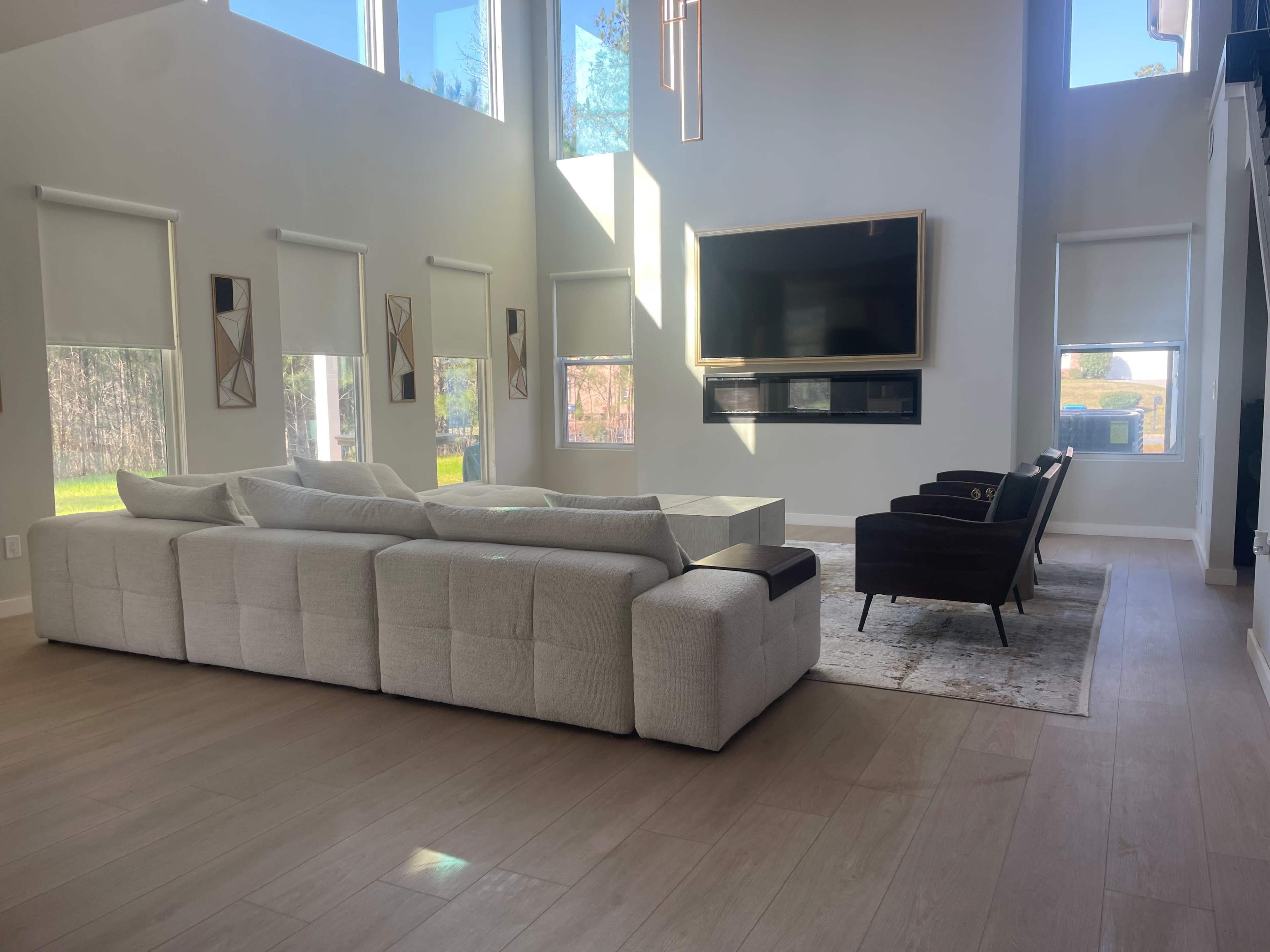 A modern living room featuring a large sectional sofa, a wall-mounted television, and two chairs positioned on a rug.