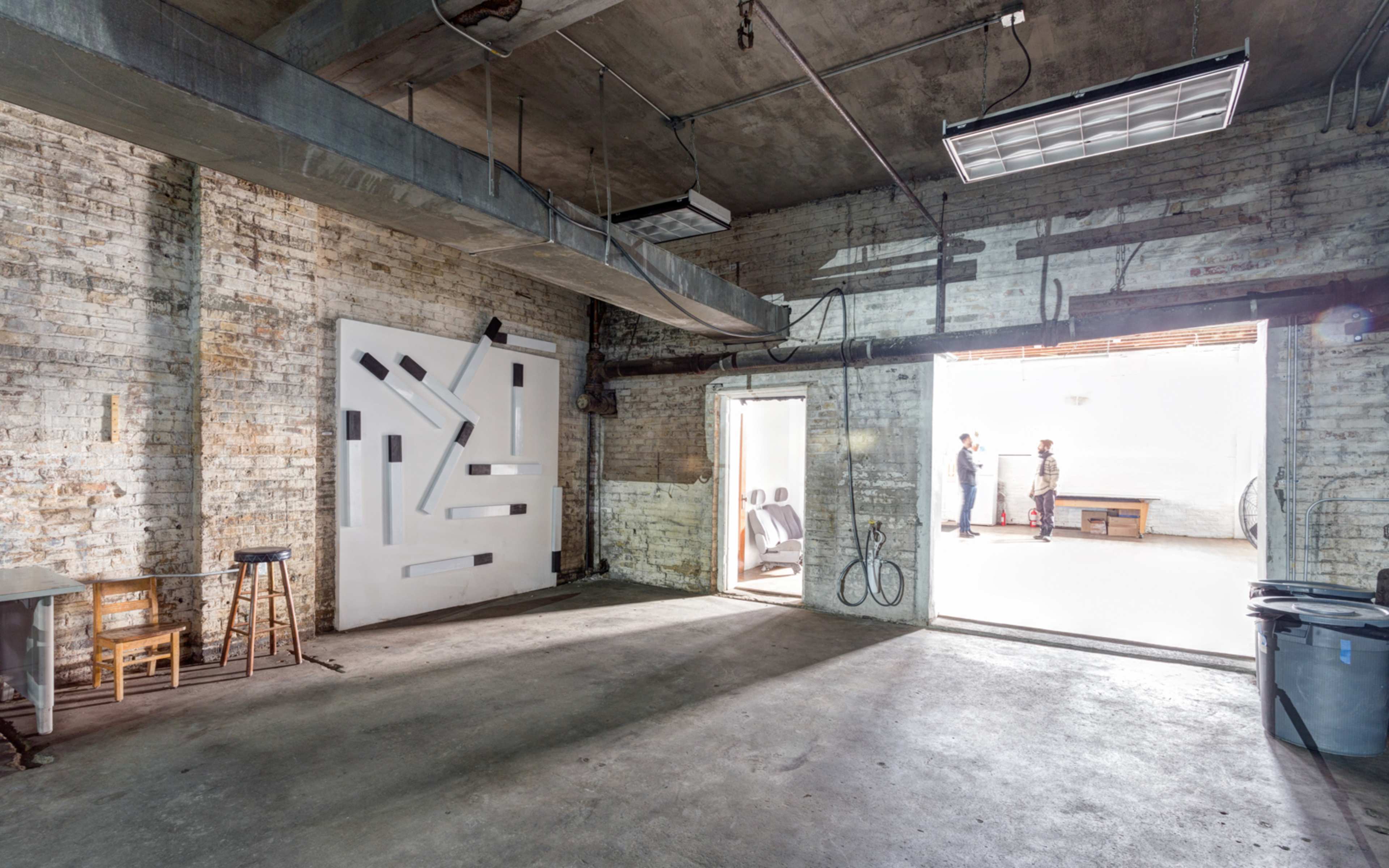 An industrial-style interior space with exposed brick walls, two doorways, and a white abstract art piece on one wall.