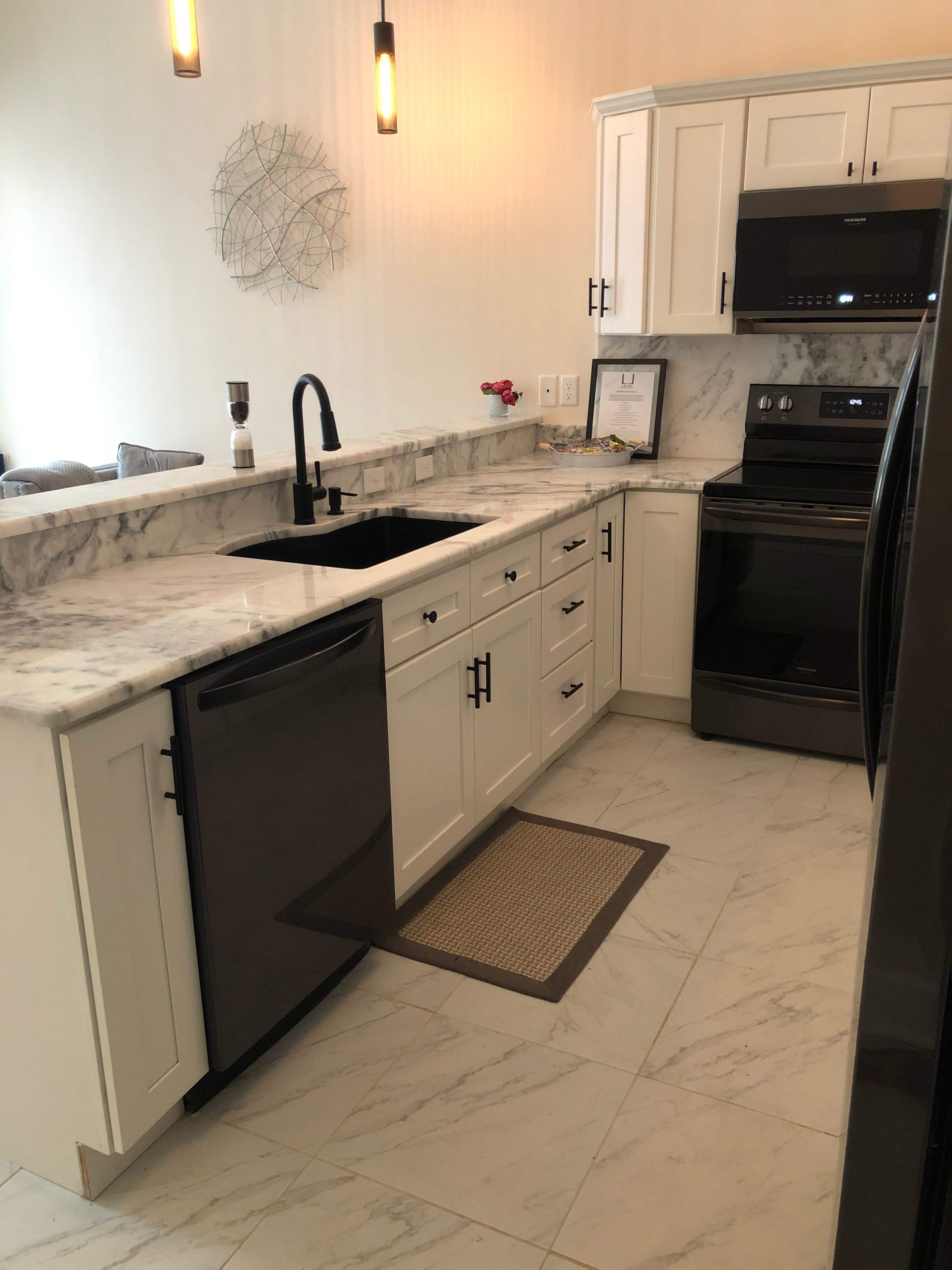 A modern kitchen featuring white cabinets, a black sink, and marble countertops with stainless steel appliances.