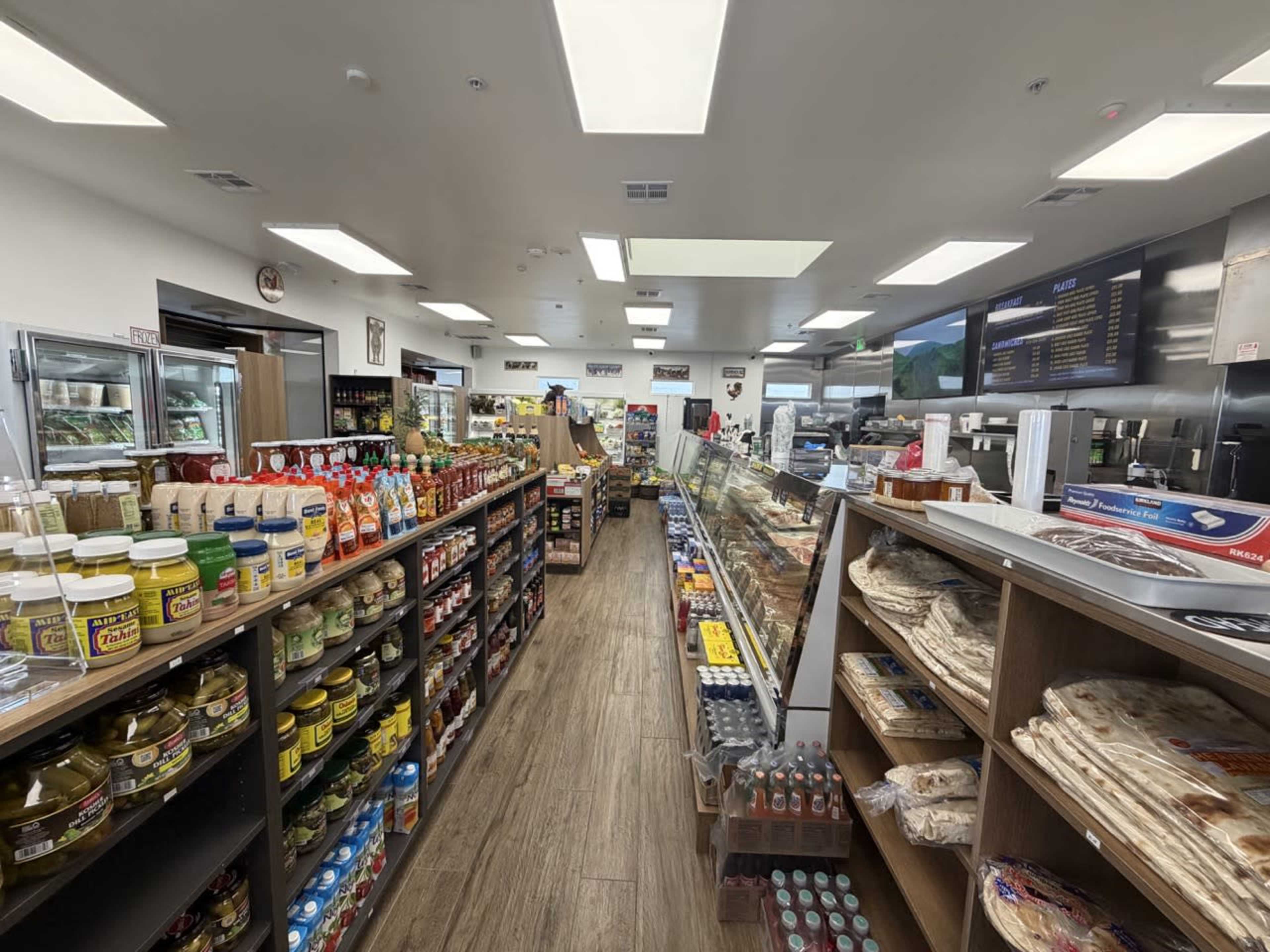 The image shows the interior of a convenience store, with shelves stocked with various food items, drinks, and condiments along a narrow aisle.