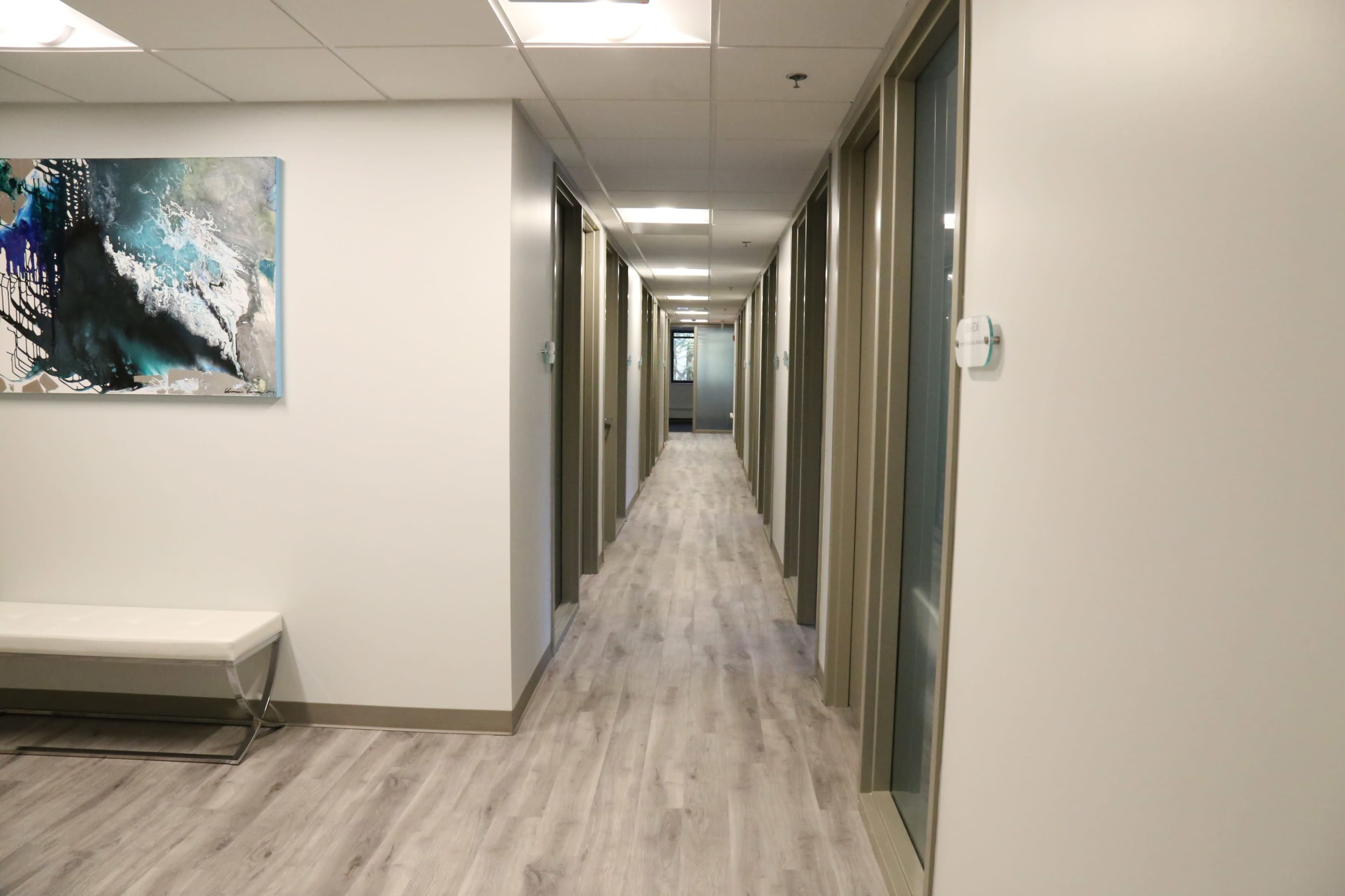 The image shows a corridor in an office building with several closed doors on either side and a bench against one wall.