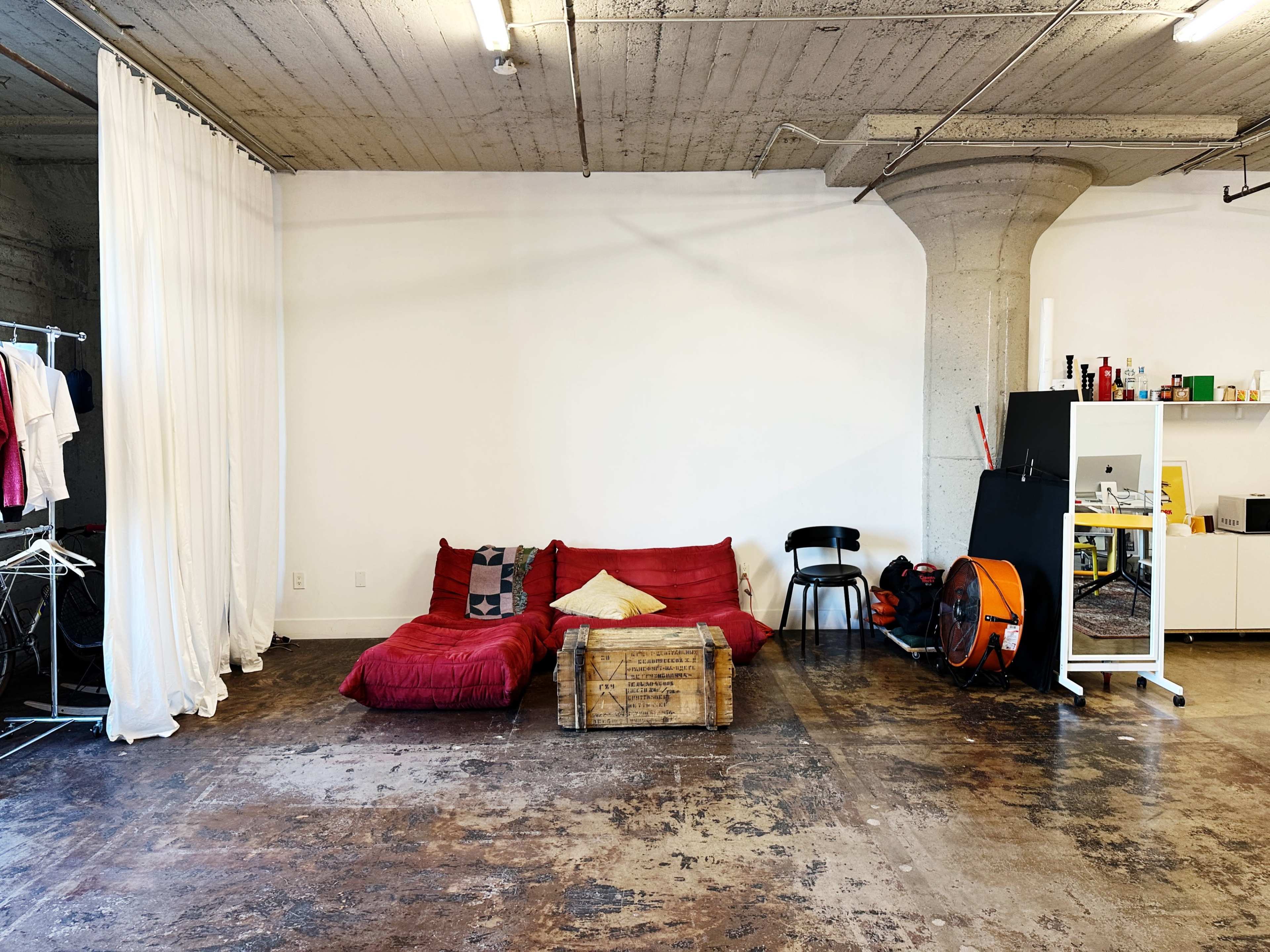 The image shows a spacious room with a red couch, a wooden coffee table, a black chair, and various storage items against the walls.