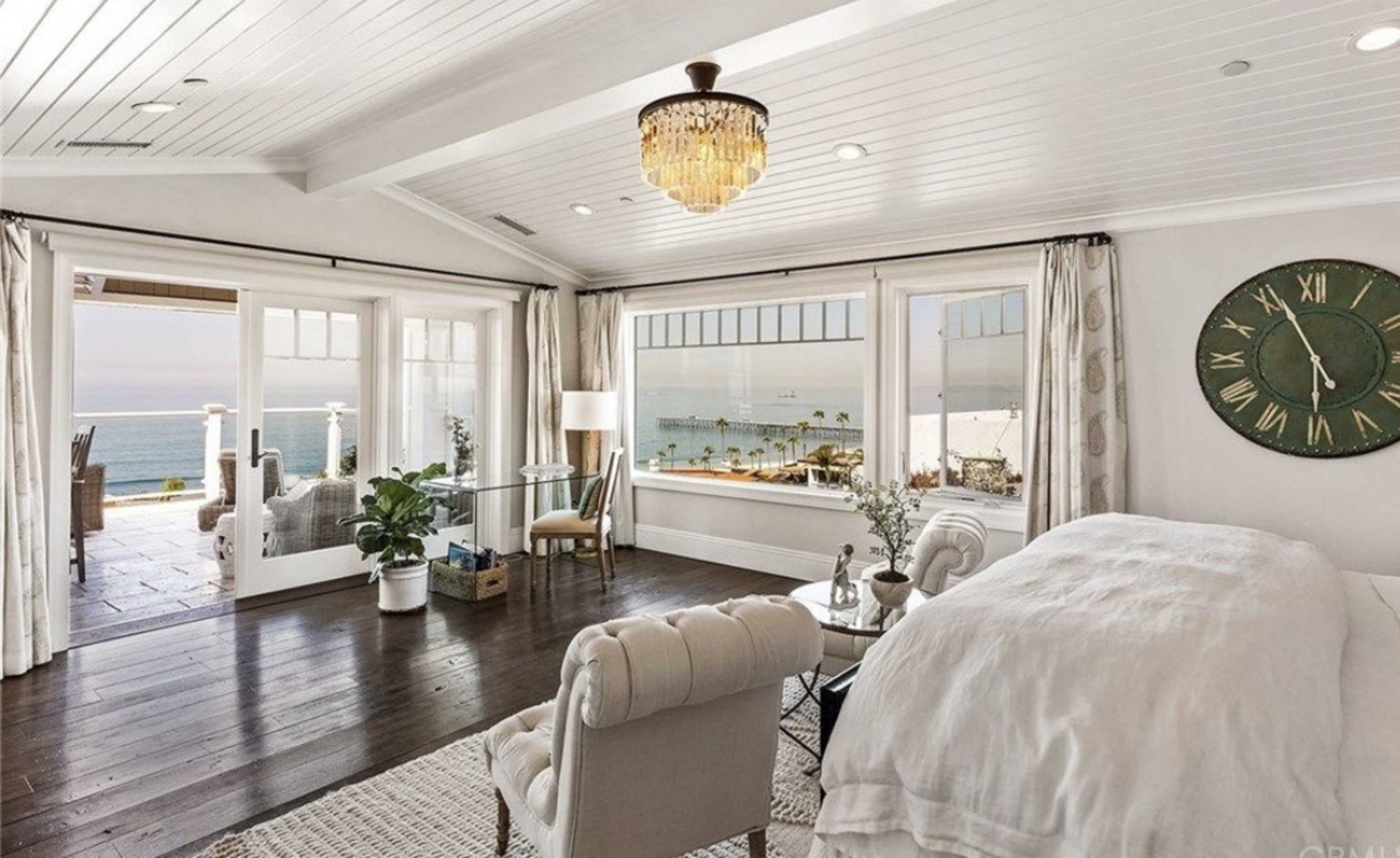 A bright and airy living room features a large window with ocean views, a chandelier, and elegant furnishings.
