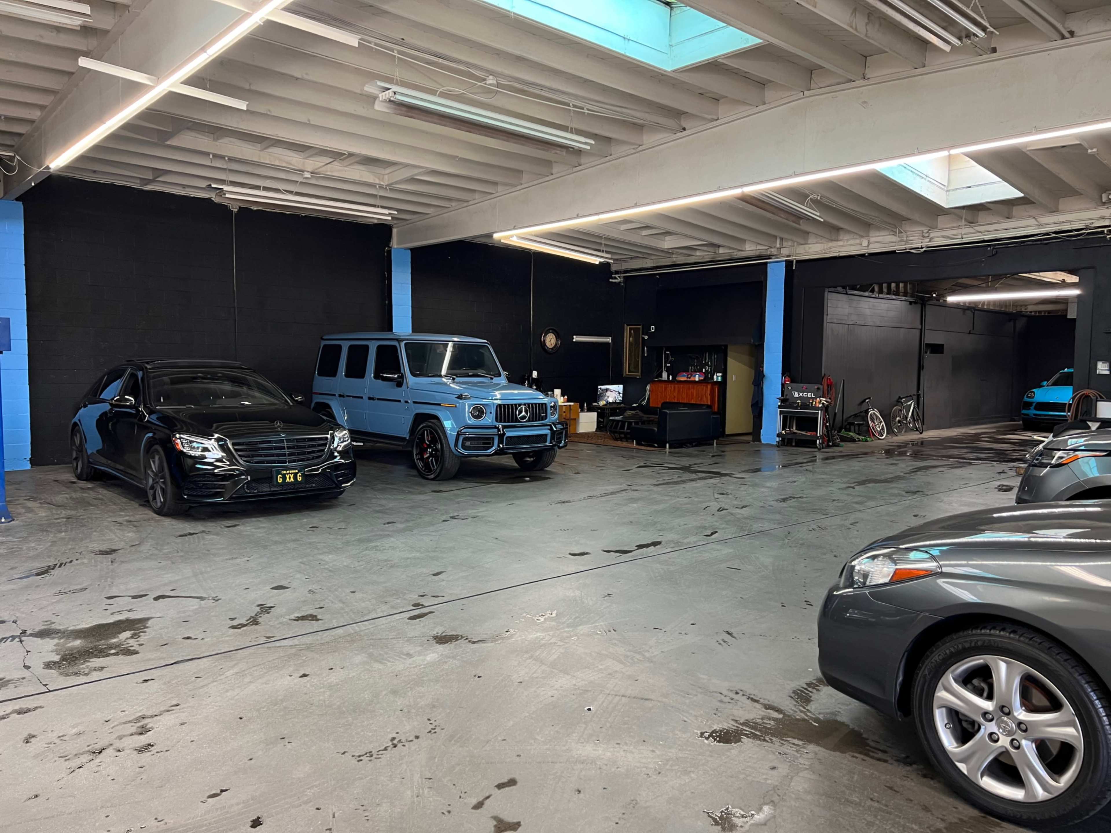 The image shows a garage with several parked cars, including a black sedan and a light blue SUV, against a backdrop of blue and black walls.