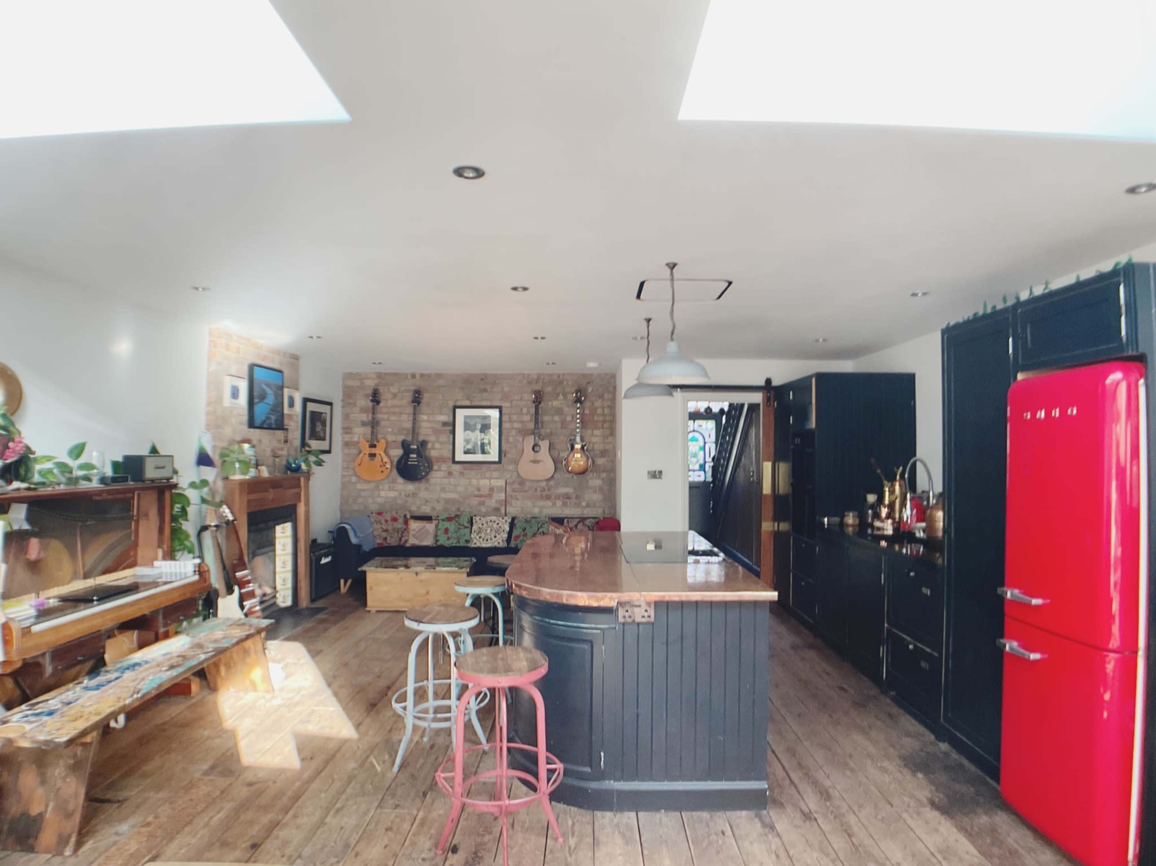A spacious kitchen and living area featuring a bar counter, wooden flooring, a red refrigerator, and several guitars displayed on the walls.