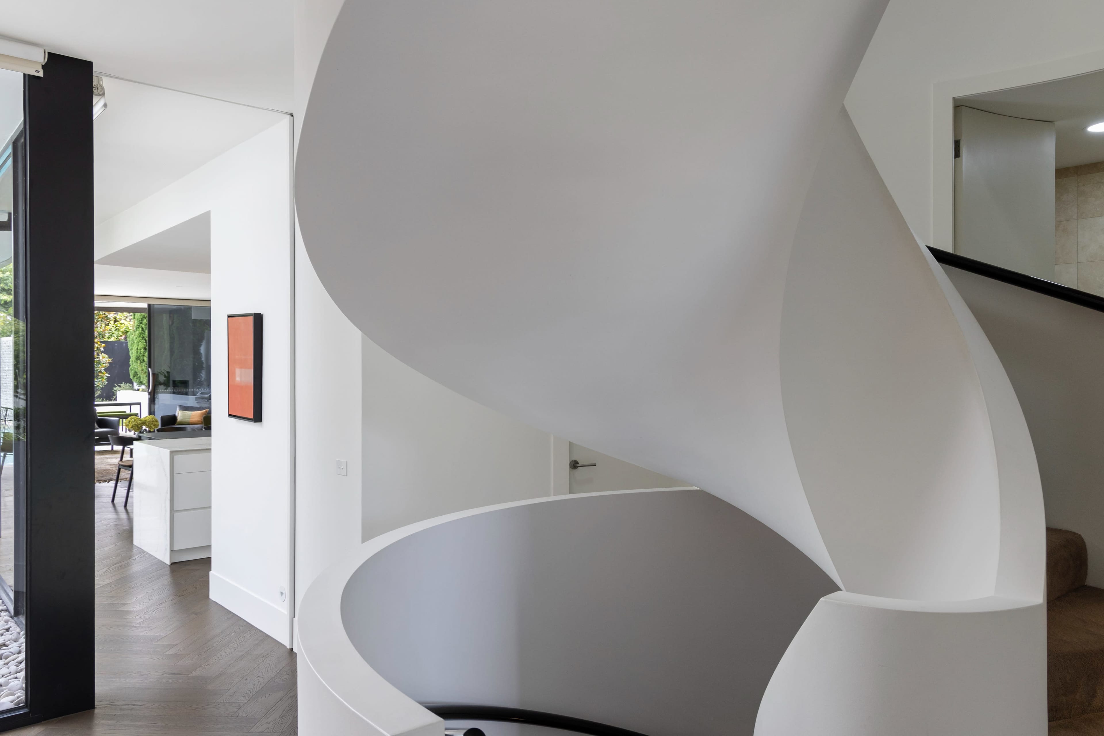 A sleek, modern spiral staircase with a white finish, leading from an upper level to a lower level in a contemporary home.