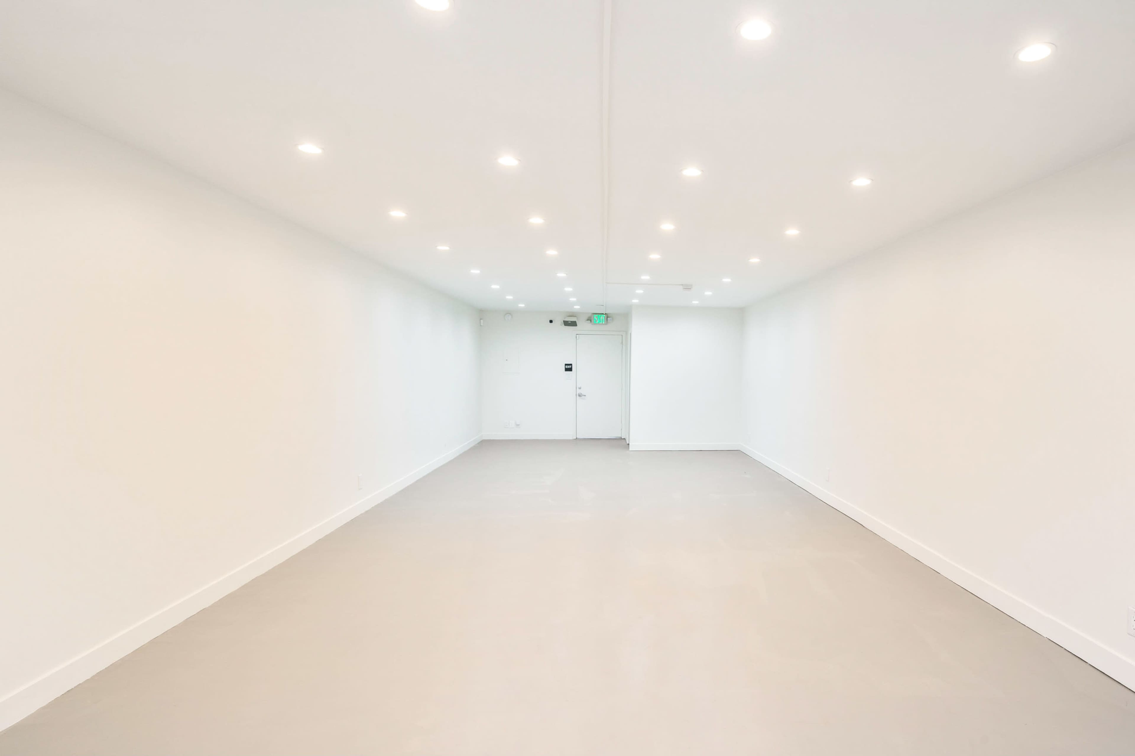 A long, empty hallway features white walls and ceiling lights, with a single door at the far end.