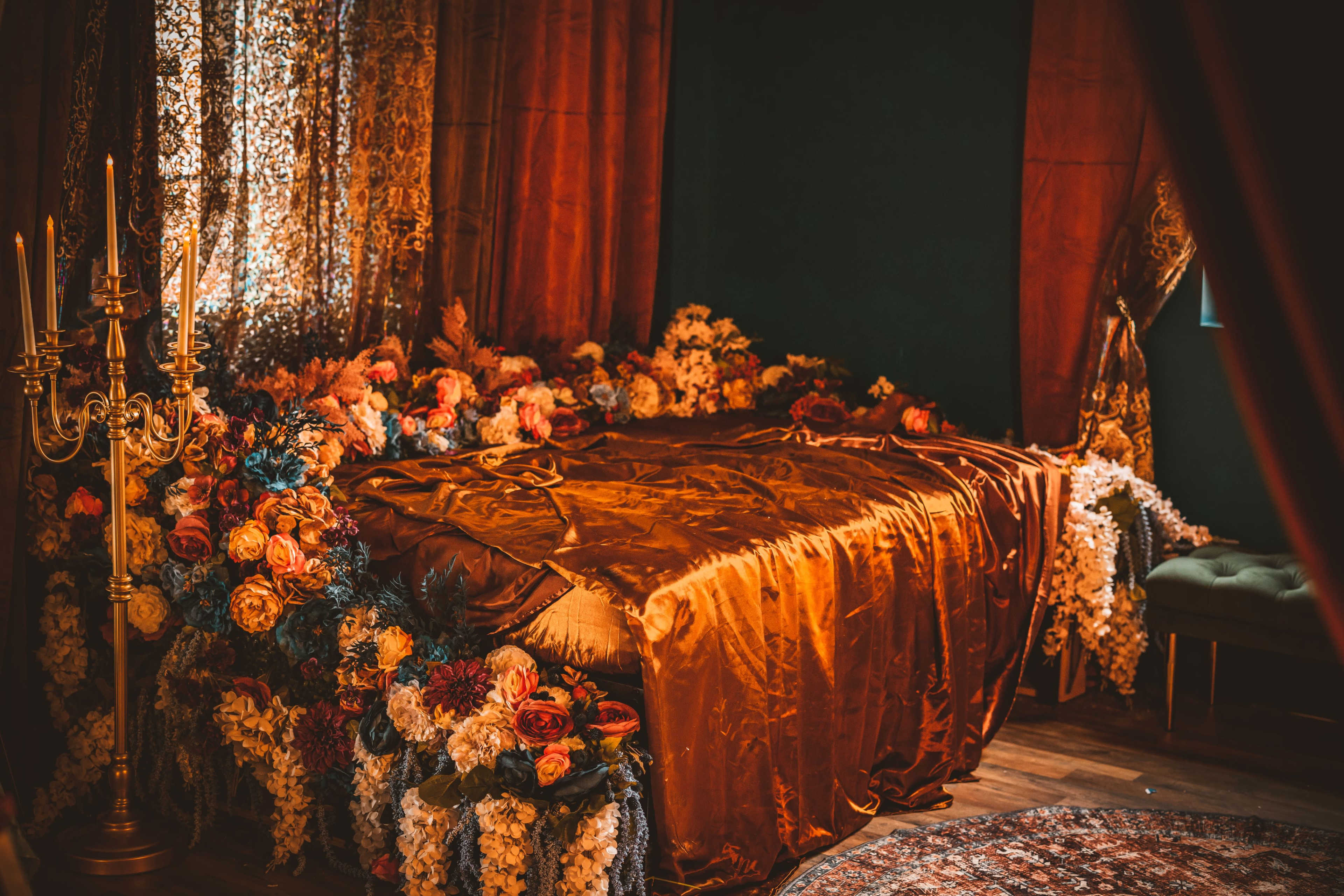 A richly decorated bedroom features a bed adorned with an ornate, flower-laden canopy and luxurious fabrics.