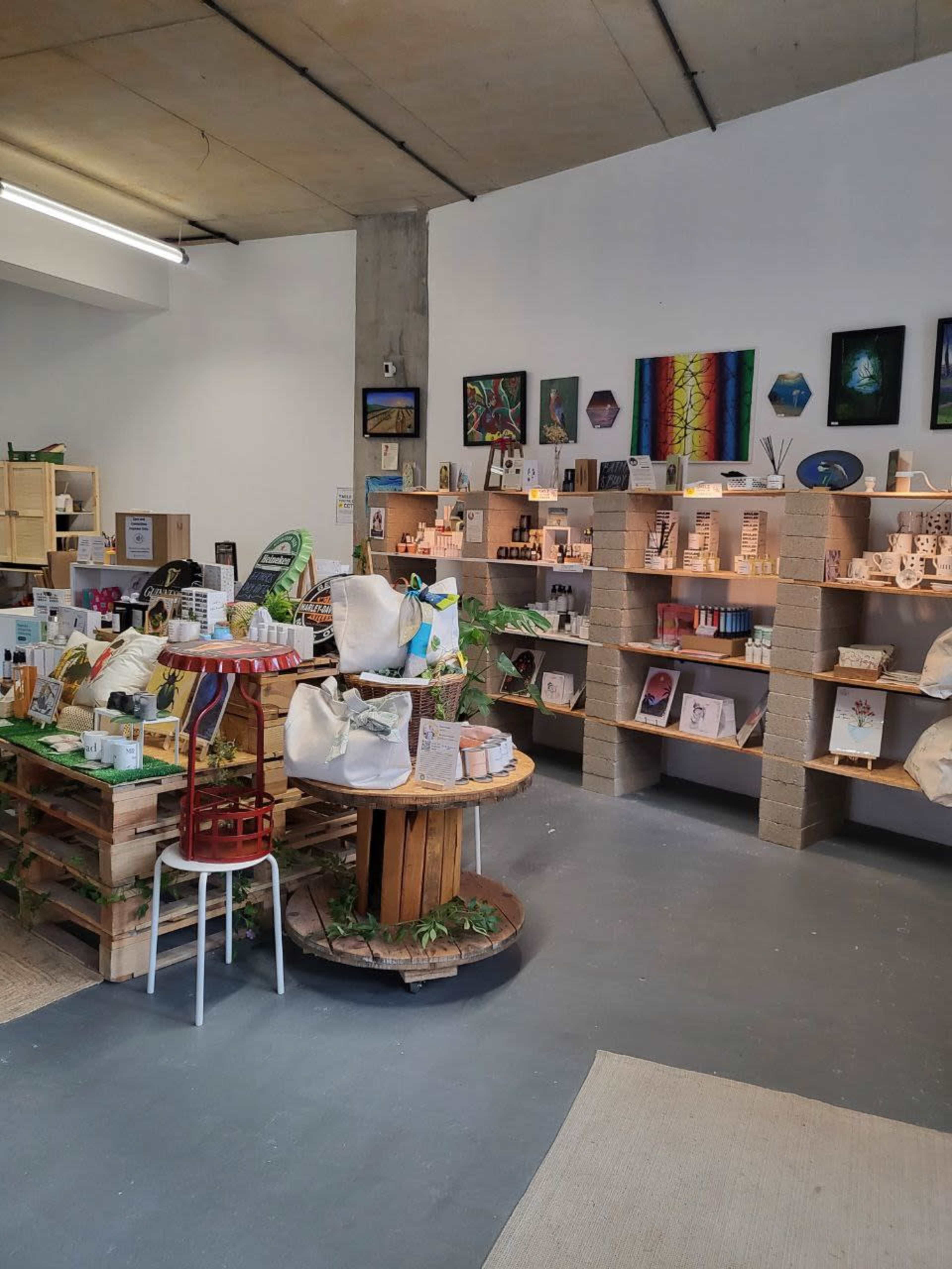 An interior of a shop featuring wooden shelves filled with various art pieces and products, along with display tables made from pallets and decorated with plants.