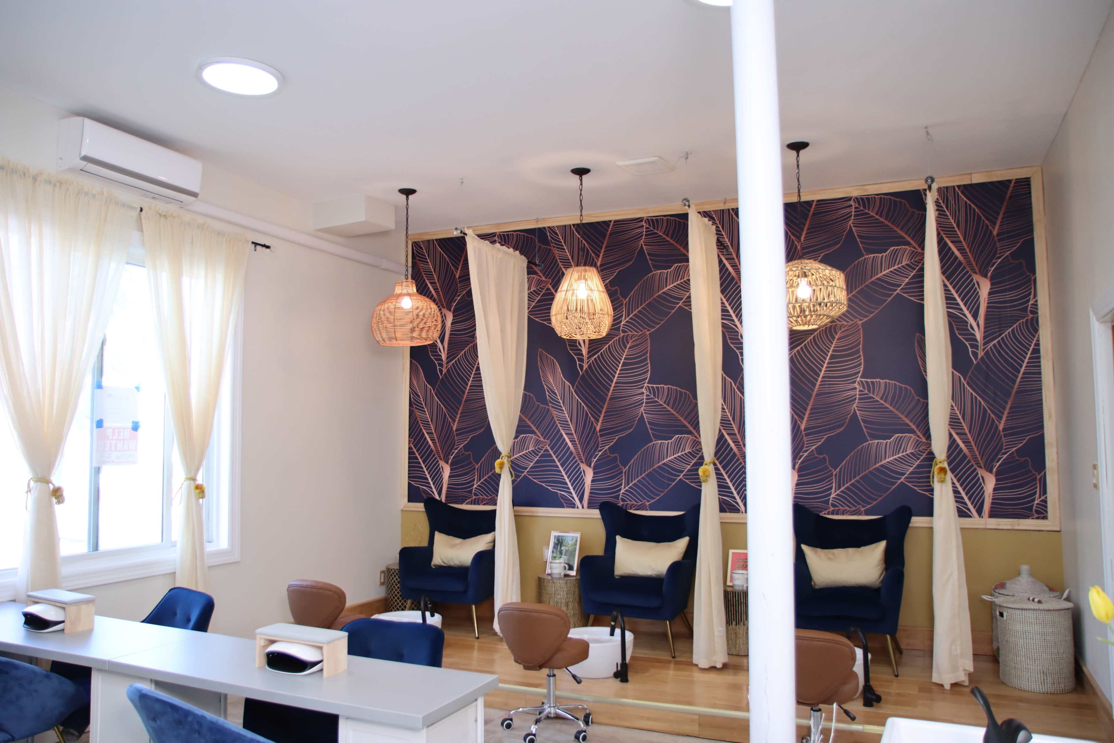 A bright salon interior featuring stylish chairs, a wall with a leaf-patterned design, and hanging light fixtures.