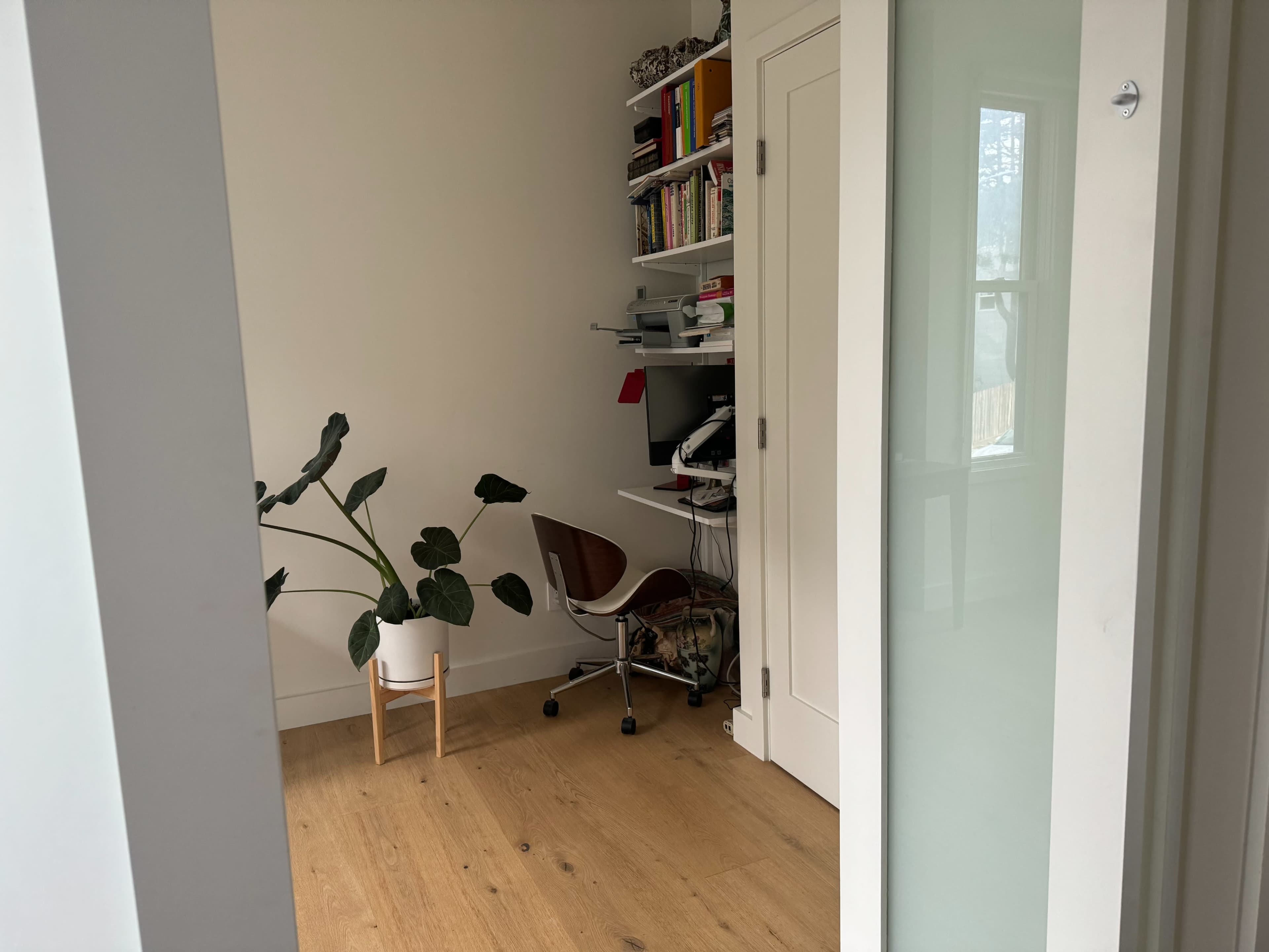 A small home office area with a plant, a chair, and a desk with a computer, visible through an open doorway.