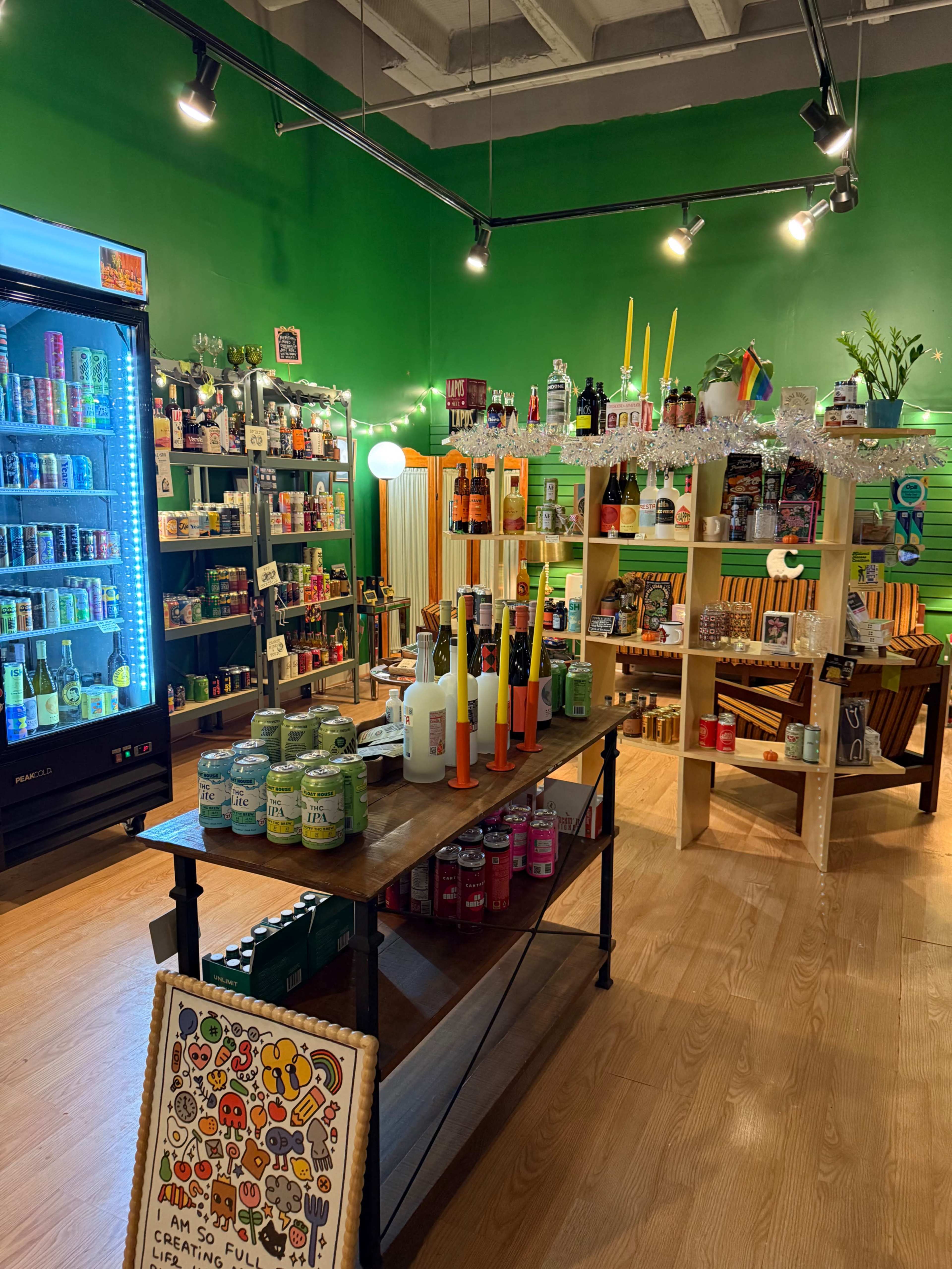 The image shows a vibrant store interior with wooden shelves stocked full of various drinks and snacks, illuminated by bright green walls and overhead lights.