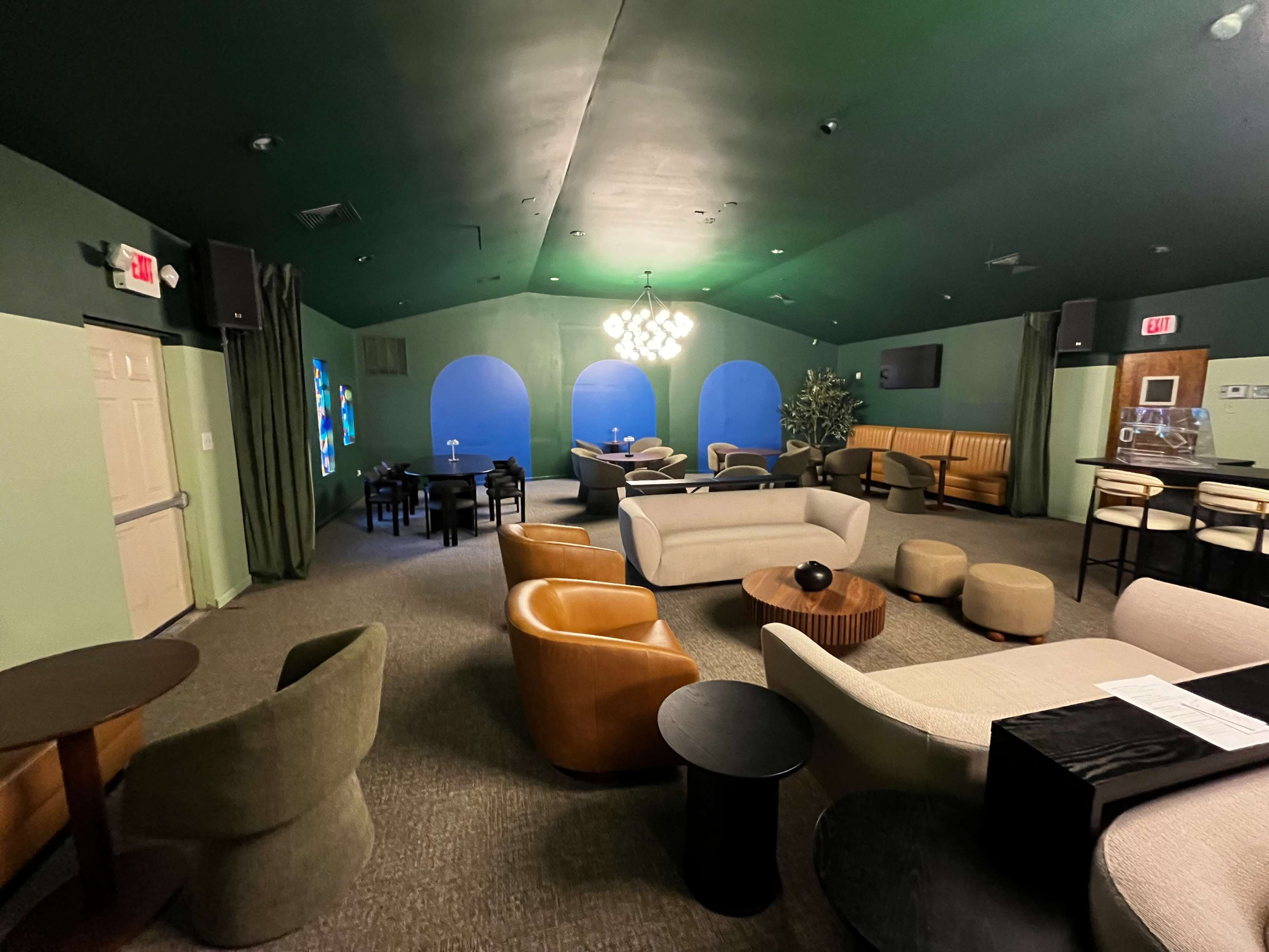 The image shows a lounge area with various seating options, including sofas and chairs, under a green ceiling.
