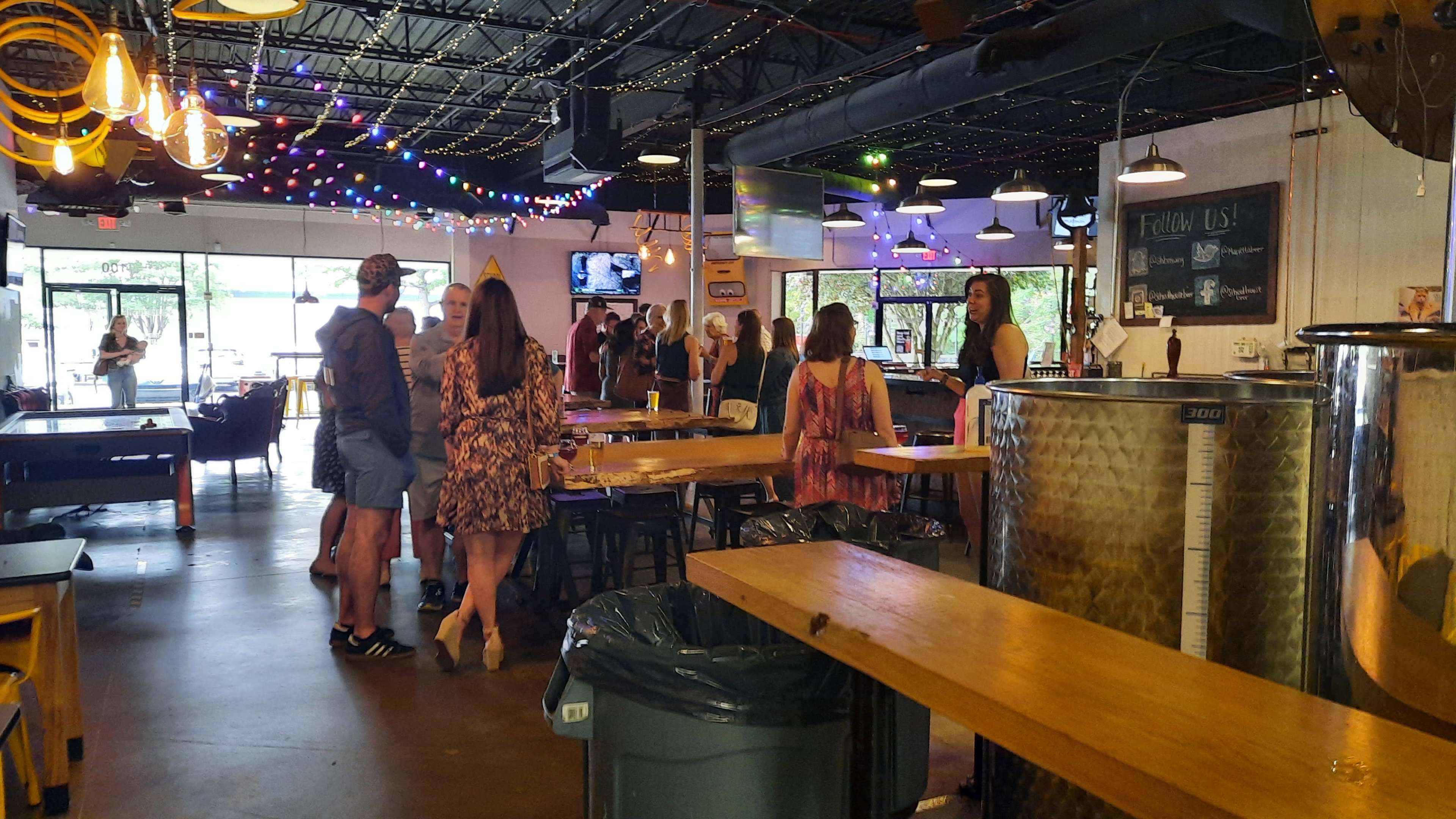 The image shows a lively bar interior with patrons mingling and colorful string lights overhead.