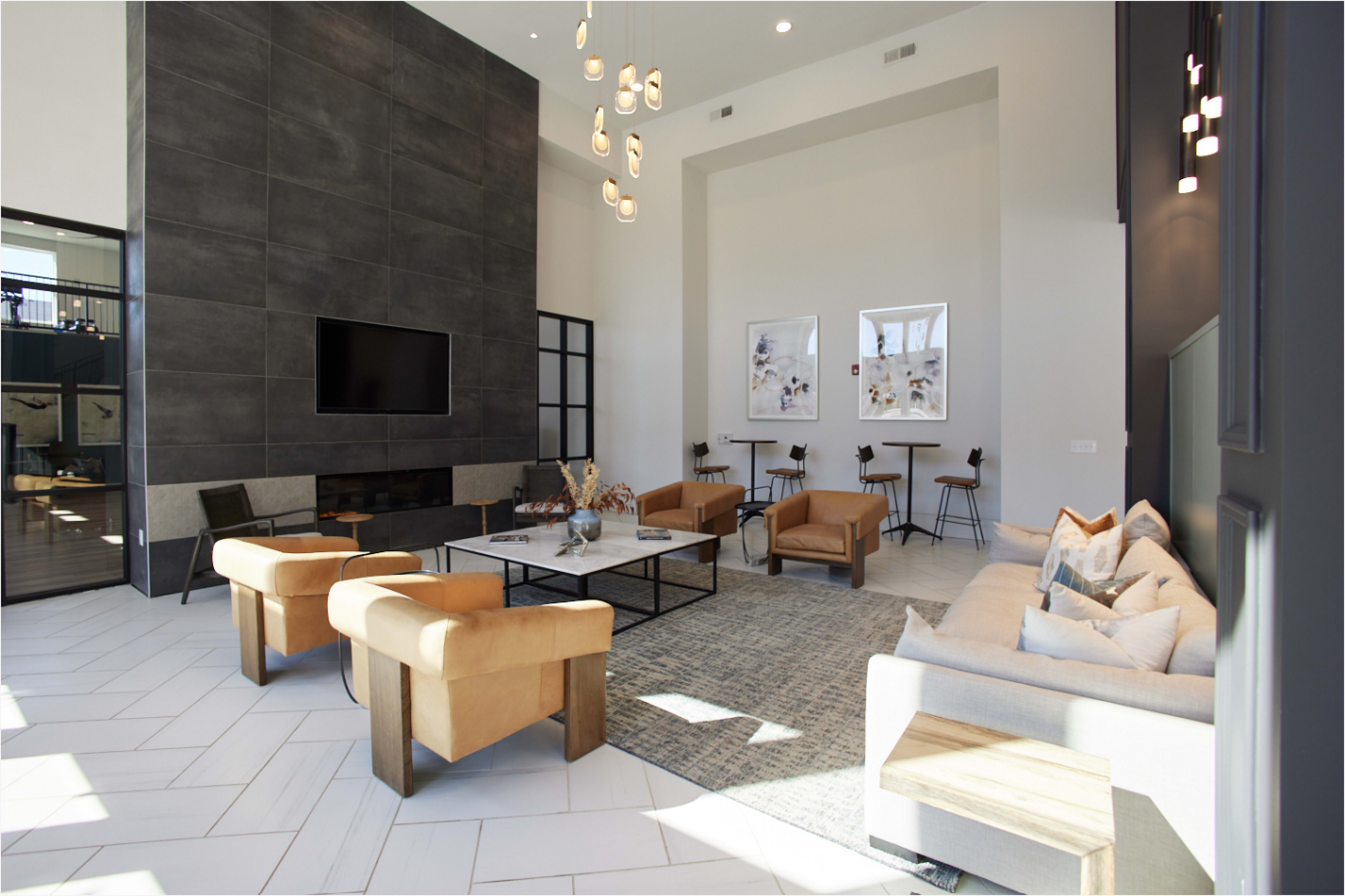 The image shows a modern, spacious living area featuring a large flat-screen TV, elegant seating arrangements, and a decorative rug.