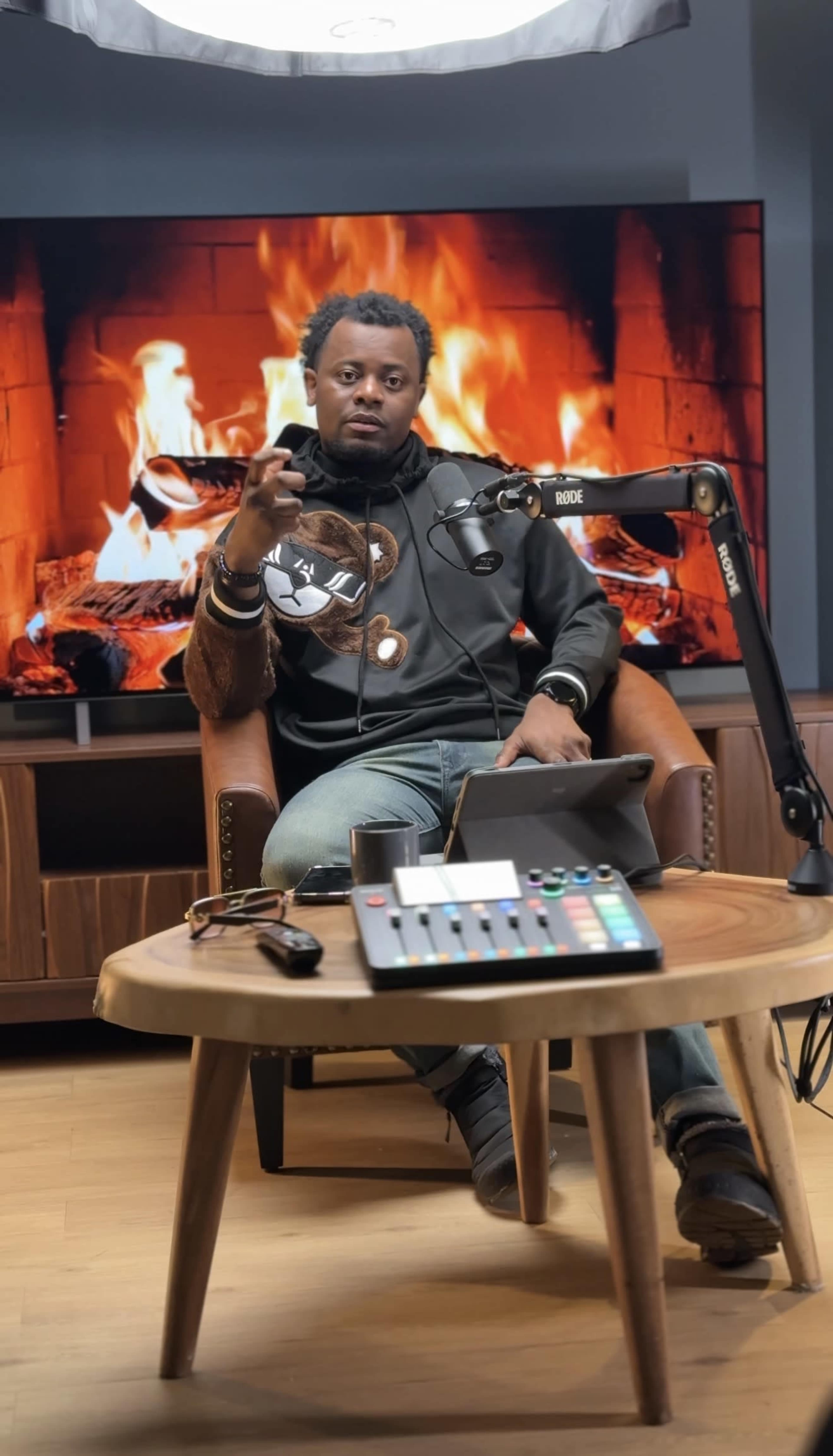 A person sits in a chair in front of a screen displaying a fireplace, with a microphone and control panel on a table nearby.