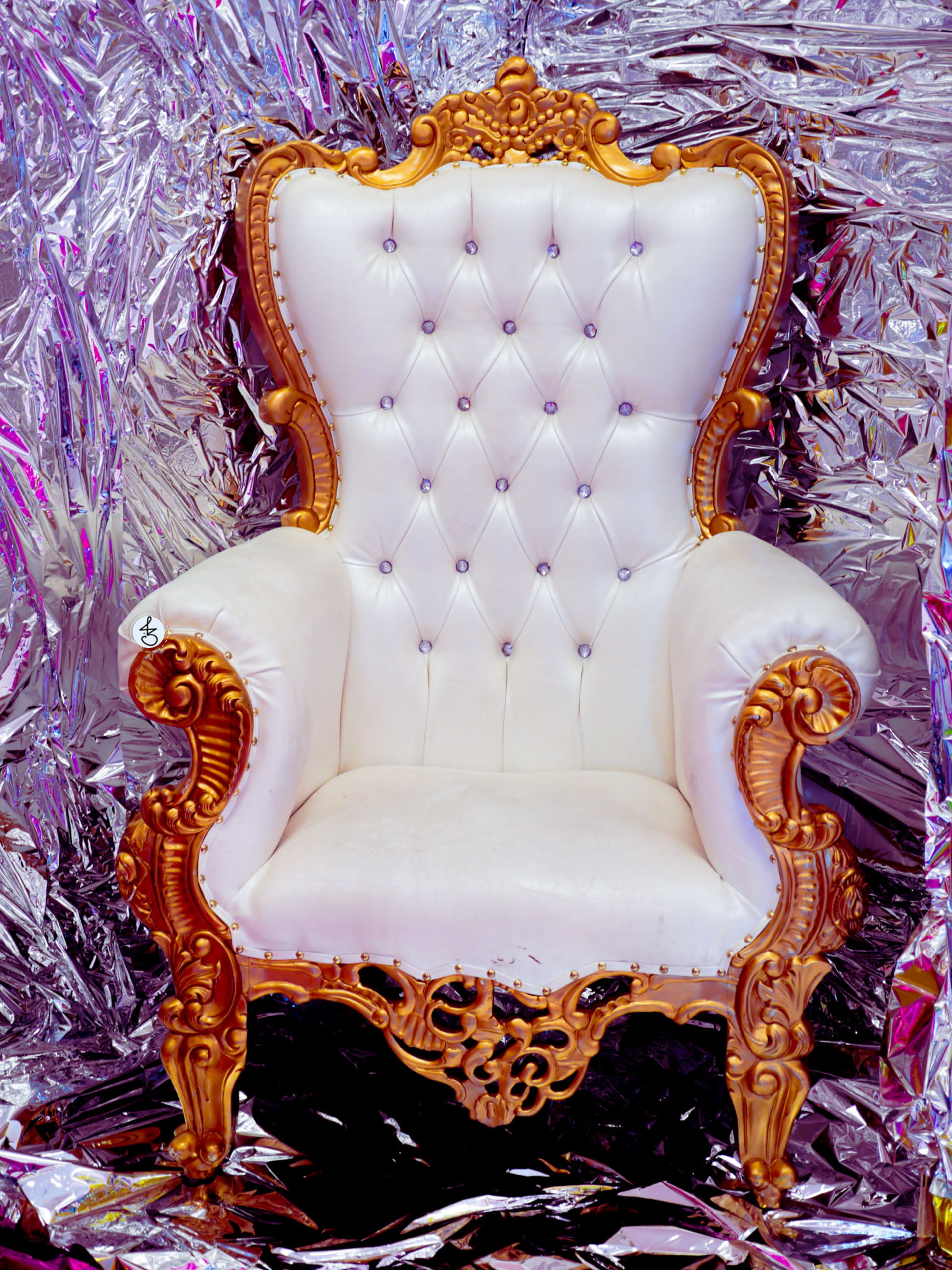 The image features a white, tufted high-back chair with ornate gold detailing set against a reflective silver background.