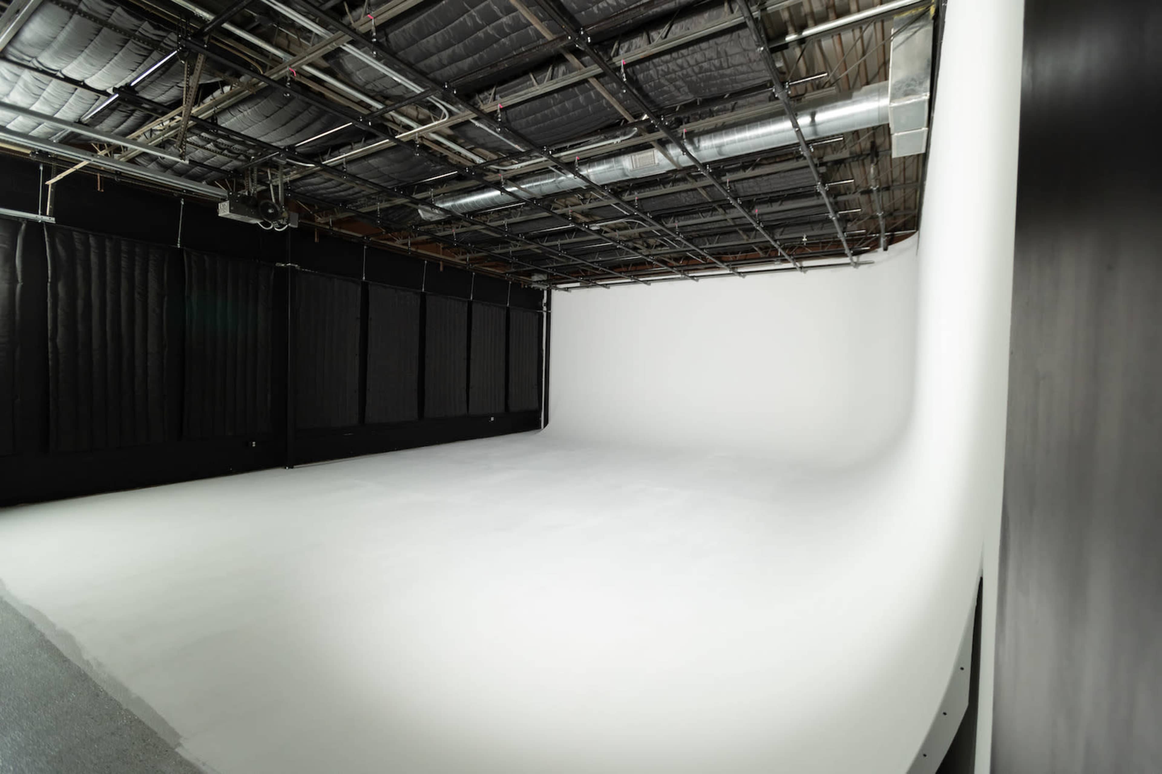 The image shows a large, empty photo studio with a curved white backdrop and overhead lighting.