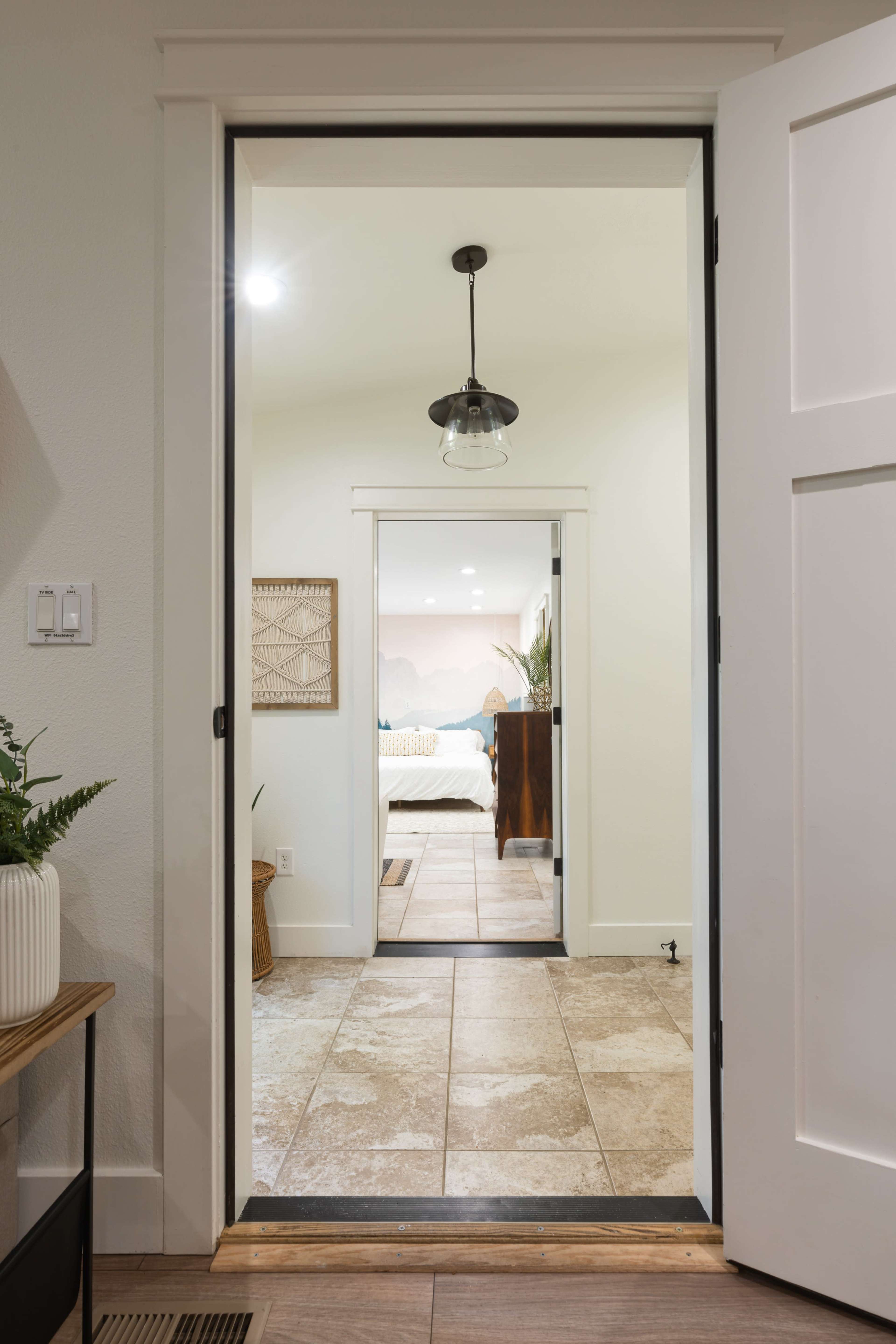 A doorway opens to a hallway leading to a bedroom, featuring a light fixture and tile flooring.