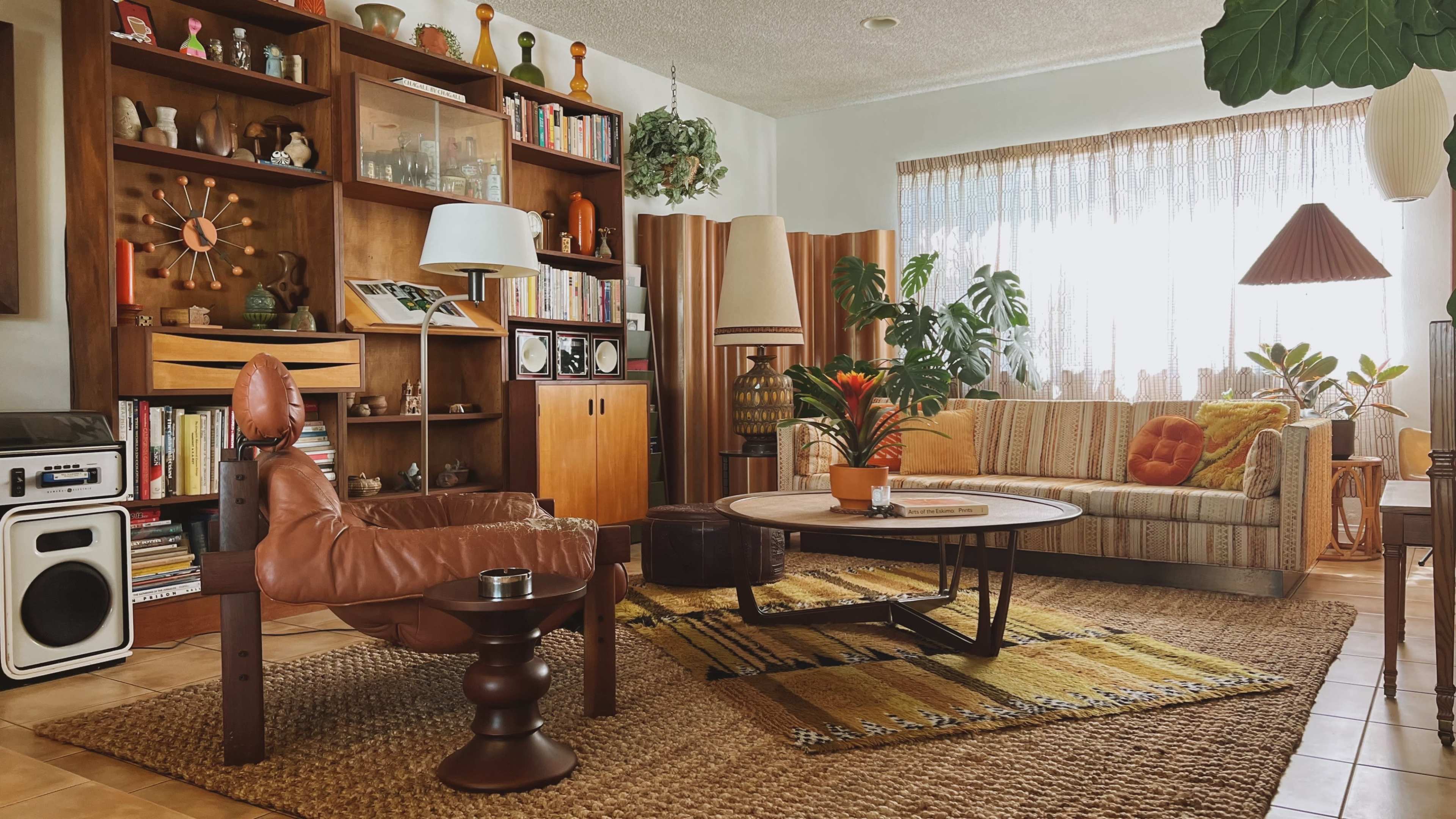 A cozy living room with a mix of wooden furniture, a patterned rug, and large windows allowing natural light to fill the space.