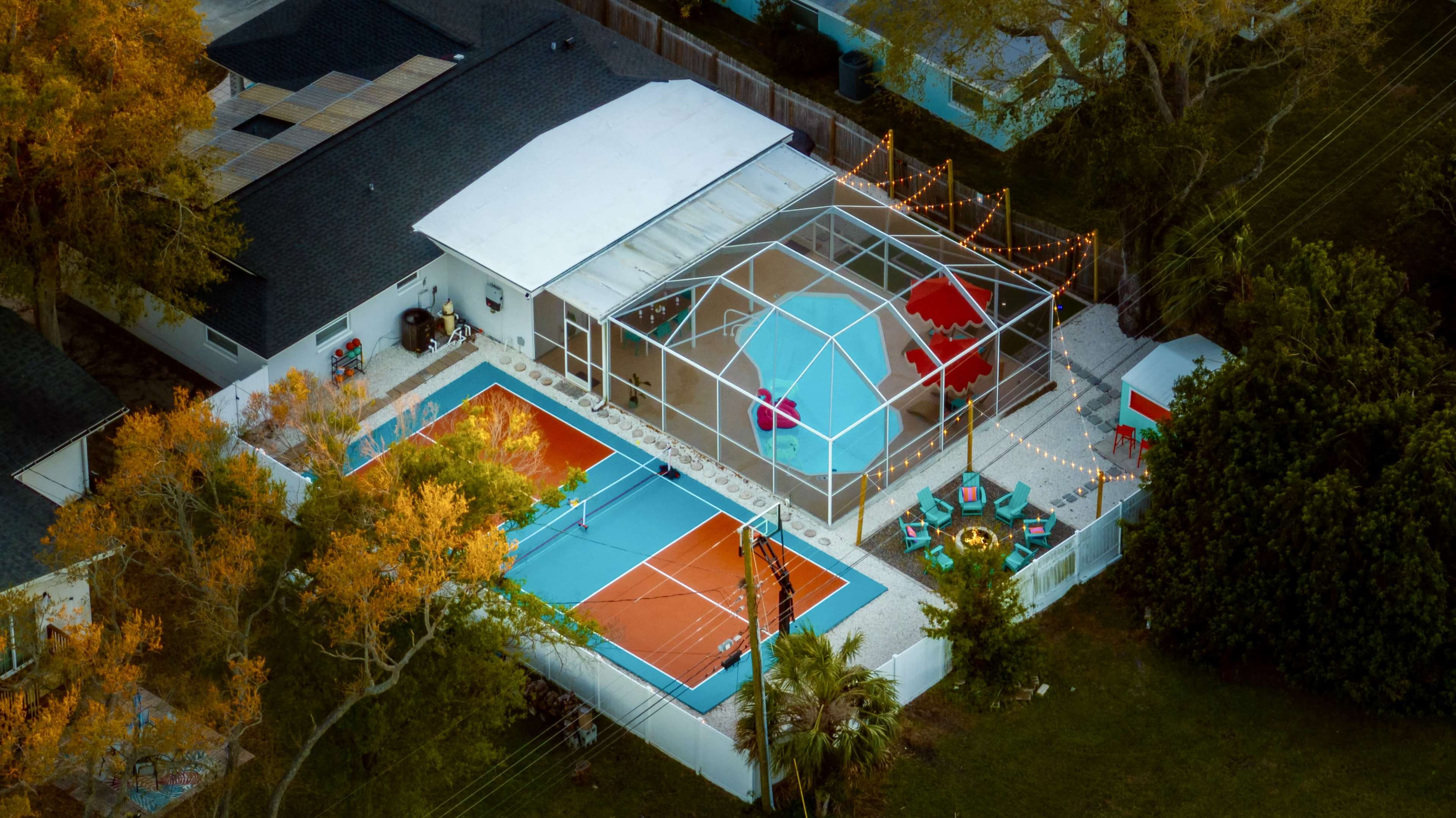 An aerial view shows a residential property featuring a swimming pool, a screened patio area, and an outdoor seating arrangement surrounded by trees.
