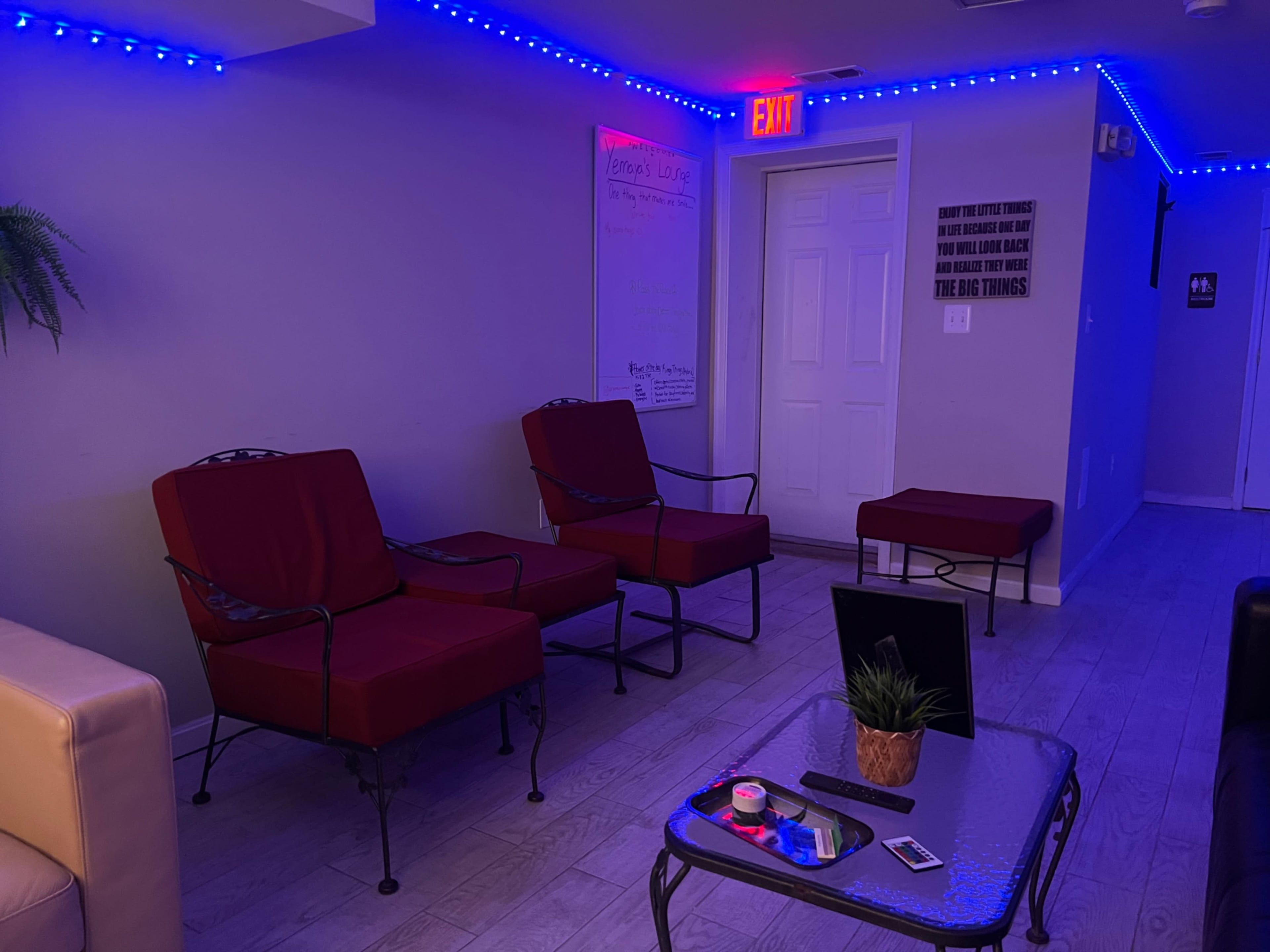 The image shows a small lounge area with two red chairs and a small table, illuminated by blue LED lights along the walls.