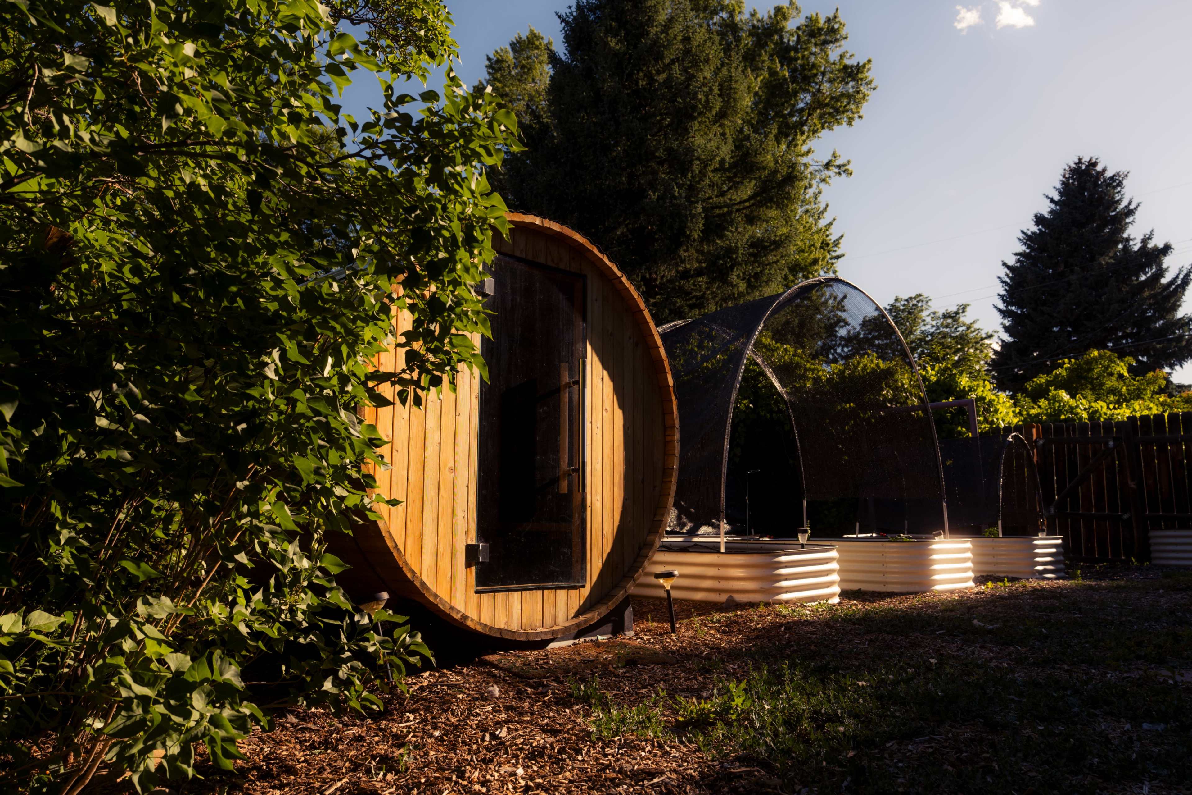 A round wooden structure sits beside a garden bed covered with a mesh canopy.