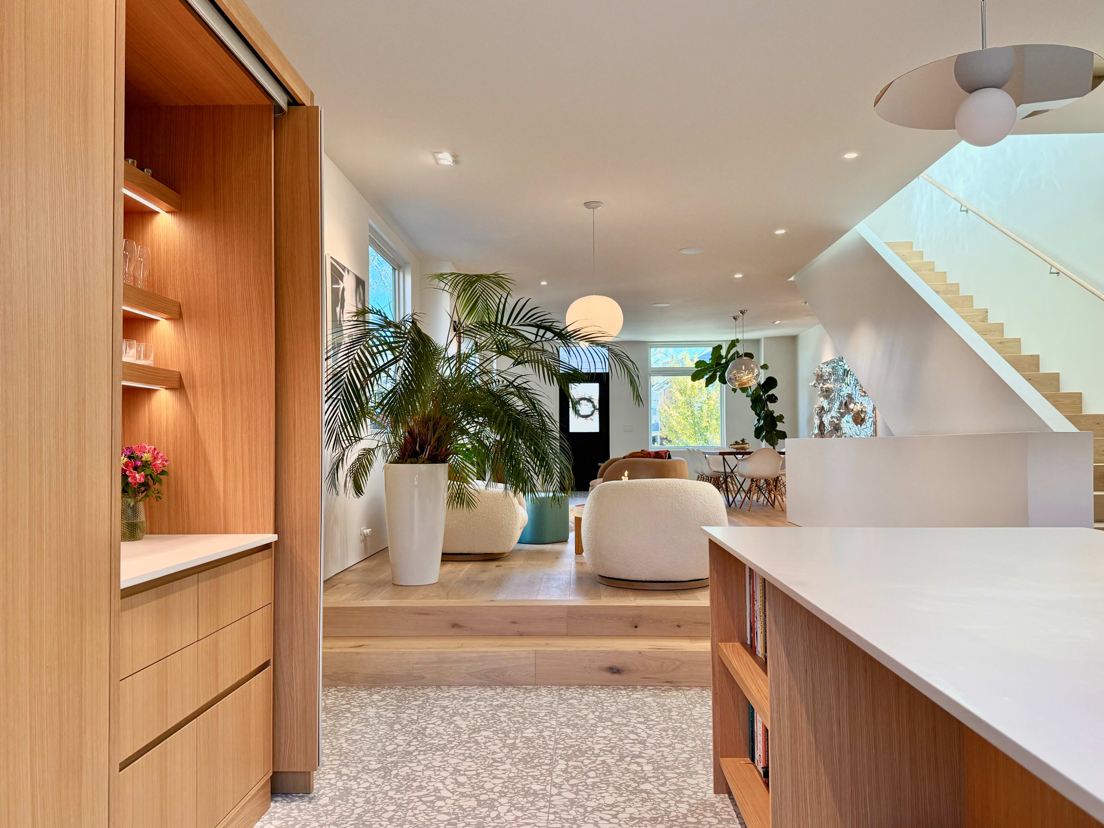 The image shows a modern open-concept living space featuring a kitchen with wooden cabinetry, a dining area, and a staircase leading to an upper level.