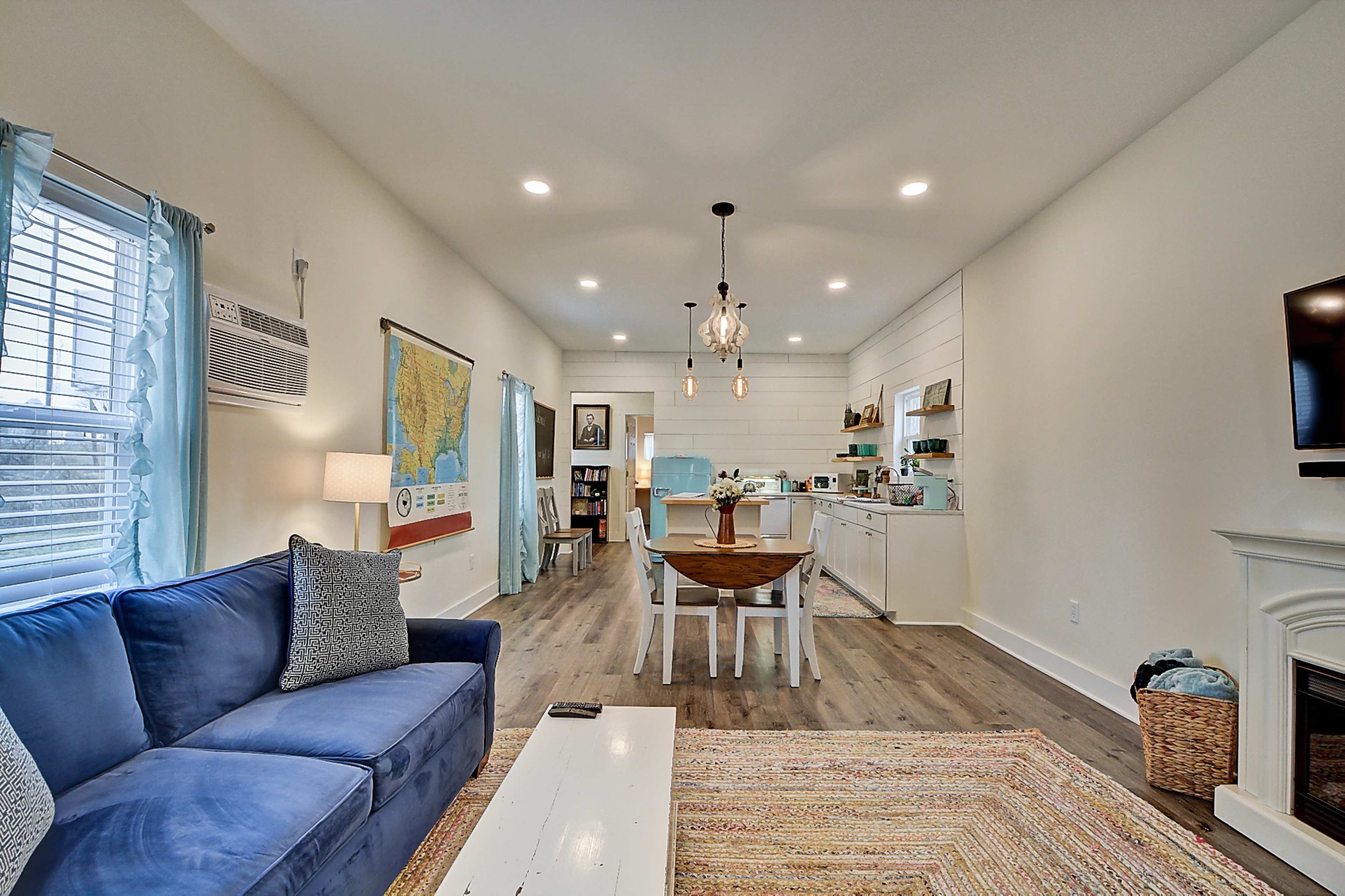 A modern, open-concept living space featuring a blue sofa, a round dining table, and a kitchen area with white cabinetry.