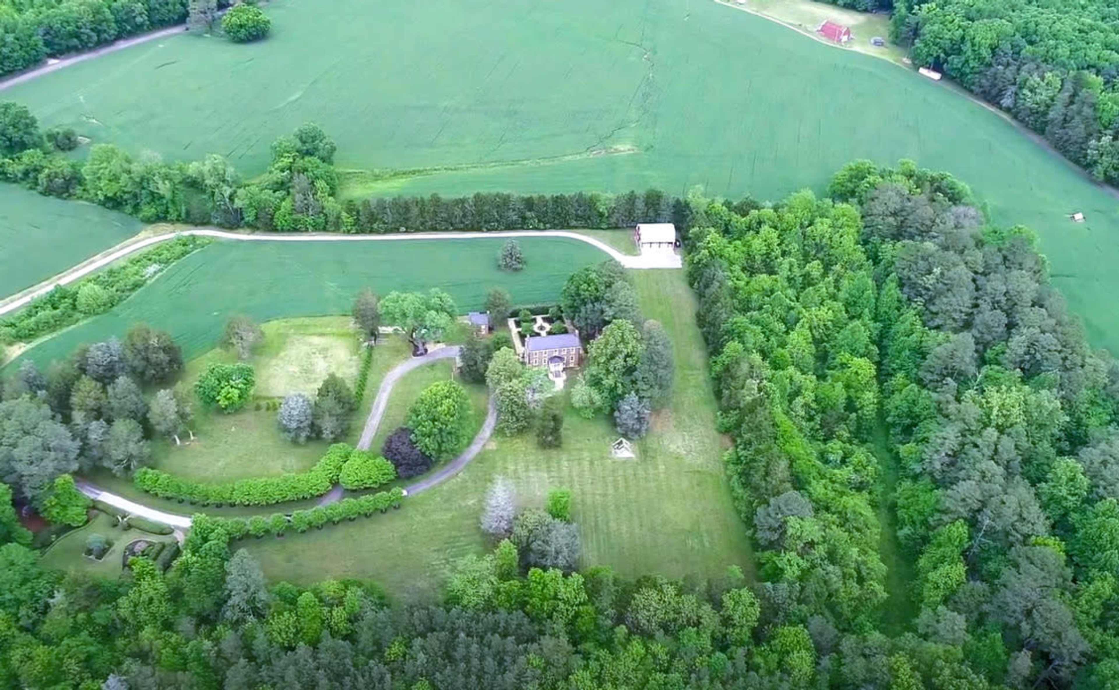 Aerial view of a large property featuring a house surrounded by neatly arranged gardens and fields of green vegetation.