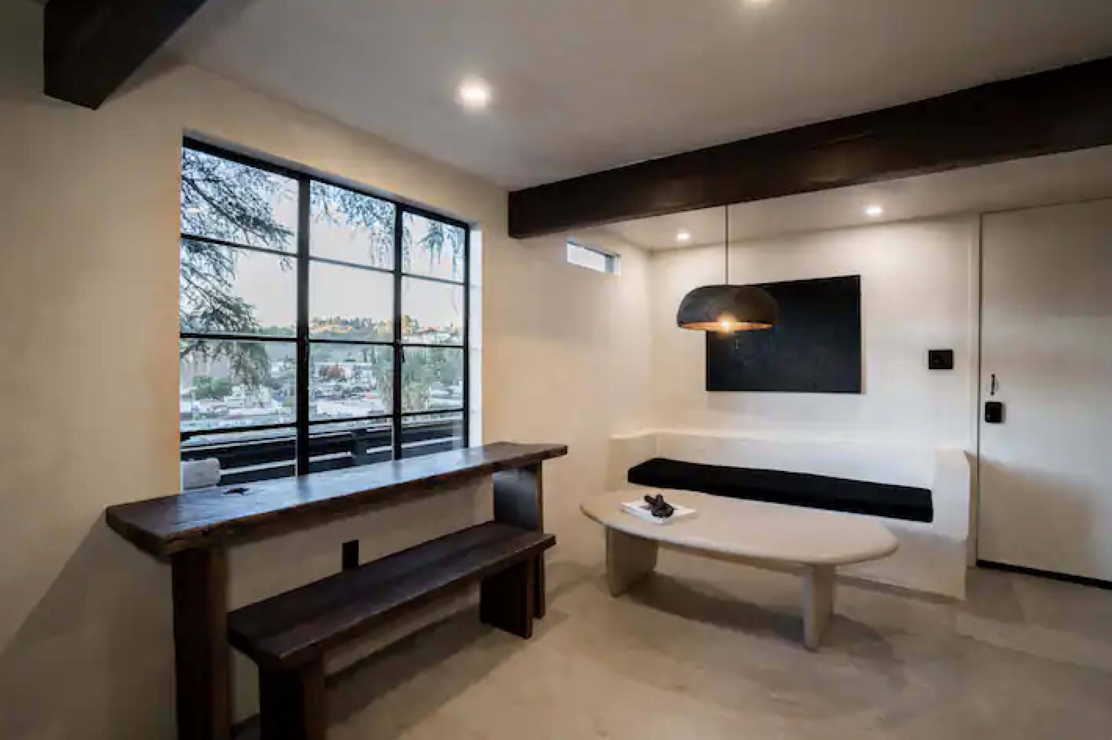 A modern, minimalistic living space with a bench, a round coffee table, and a large window offering a view of the outside.