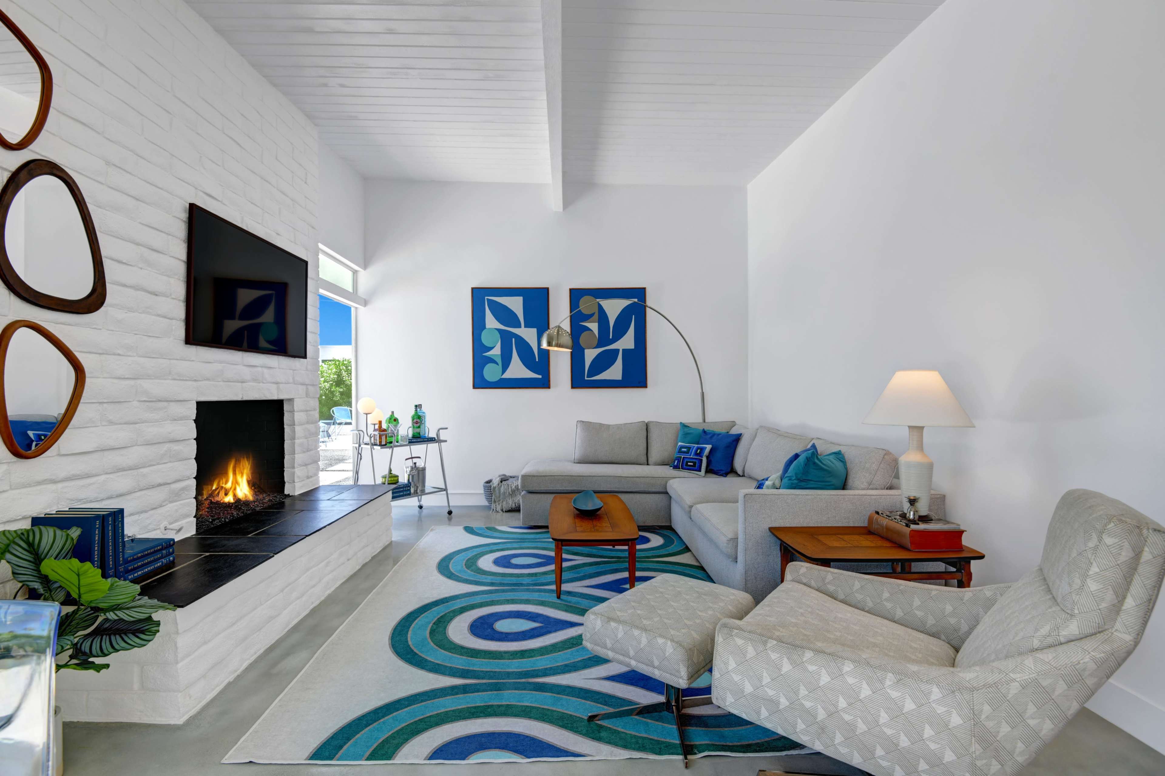 A modern living room with a white brick fireplace, a gray sofa, and colorful abstract artwork on the walls.