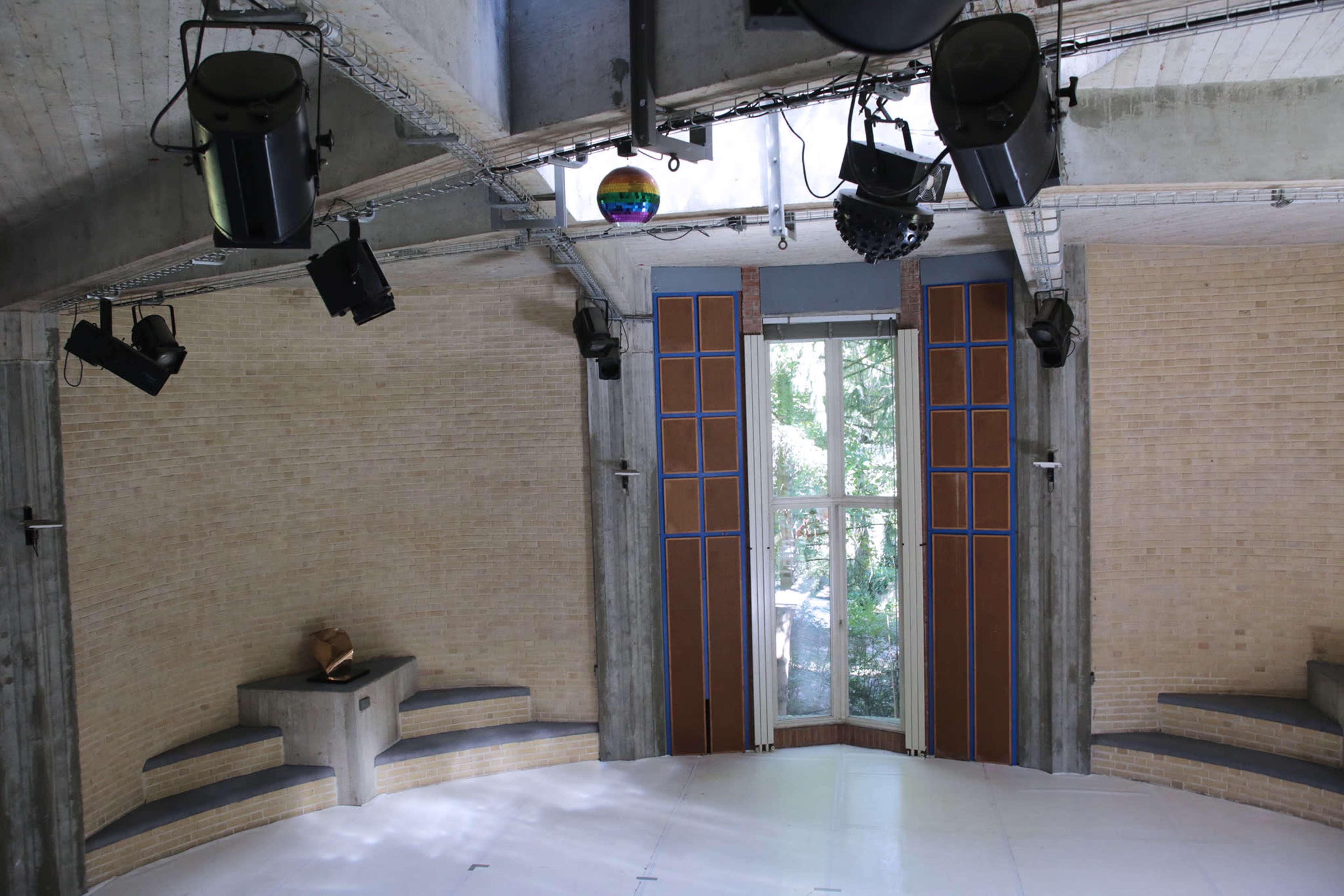 A spacious circular room with wooden doors, concrete walls, and multiple lighting fixtures mounted above.