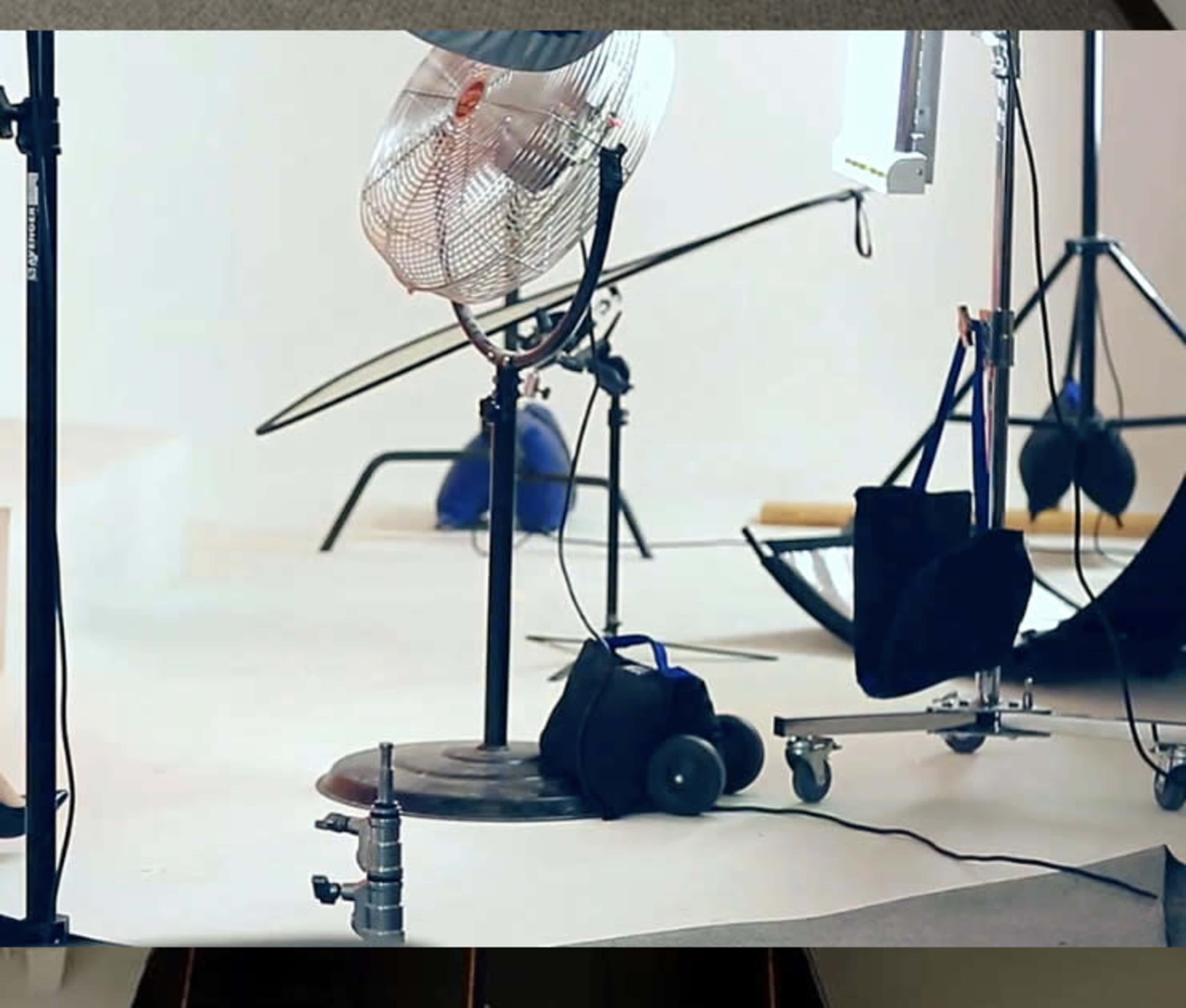 A photography studio setup featuring a fan, various lighting equipment, and backdrops on a white floor.