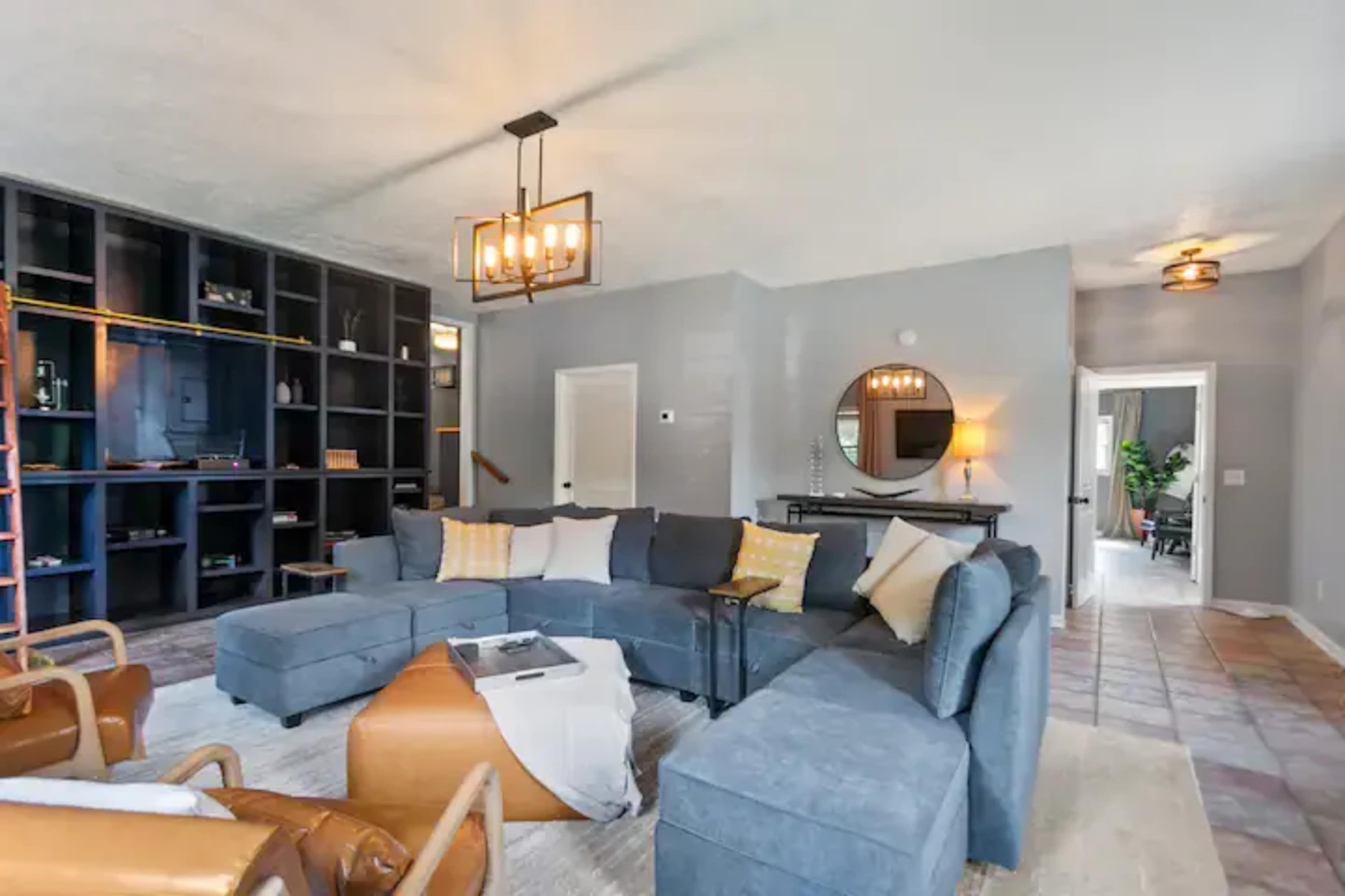 The living room features a large sectional sofa, a coffee table, a decorative wall unit, and a round mirror.
