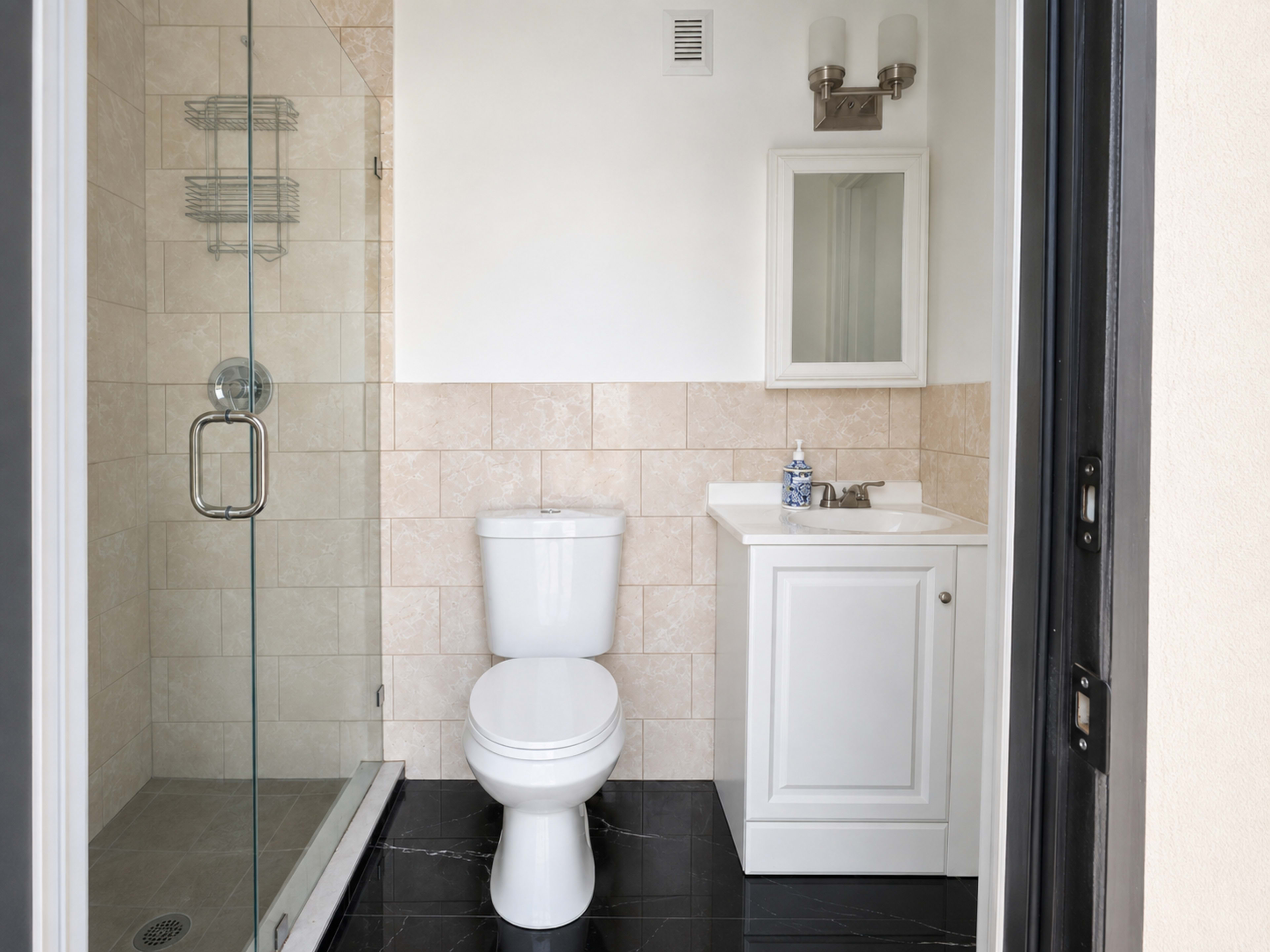 The image shows a modern bathroom featuring a clear glass shower enclosure, a toilet, and a small sink with a cabinet.