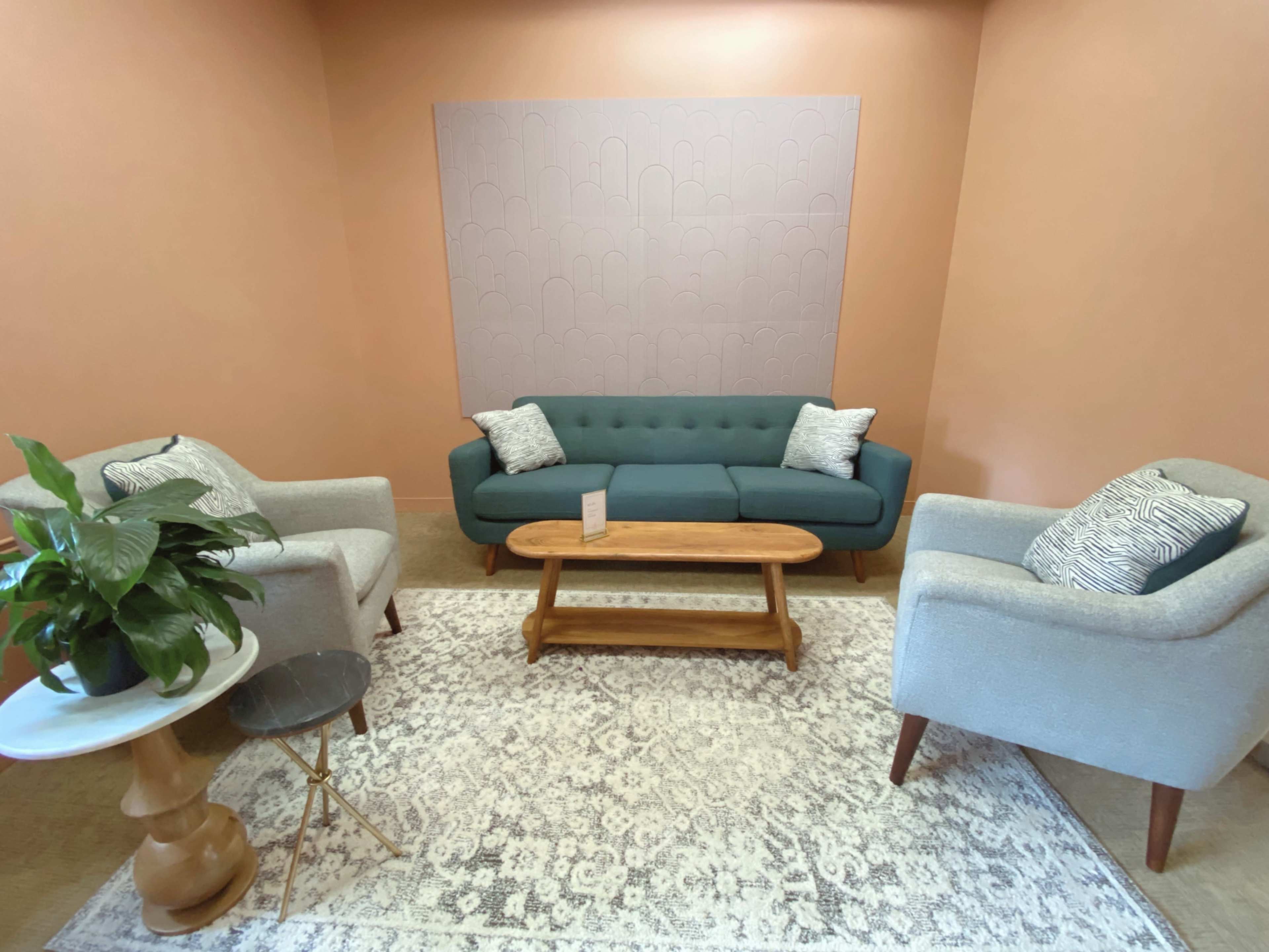 The image shows a cozy seating area with a teal sofa, two light gray armchairs, a wooden coffee table, and a small round side table, all set against a peach-colored wall.