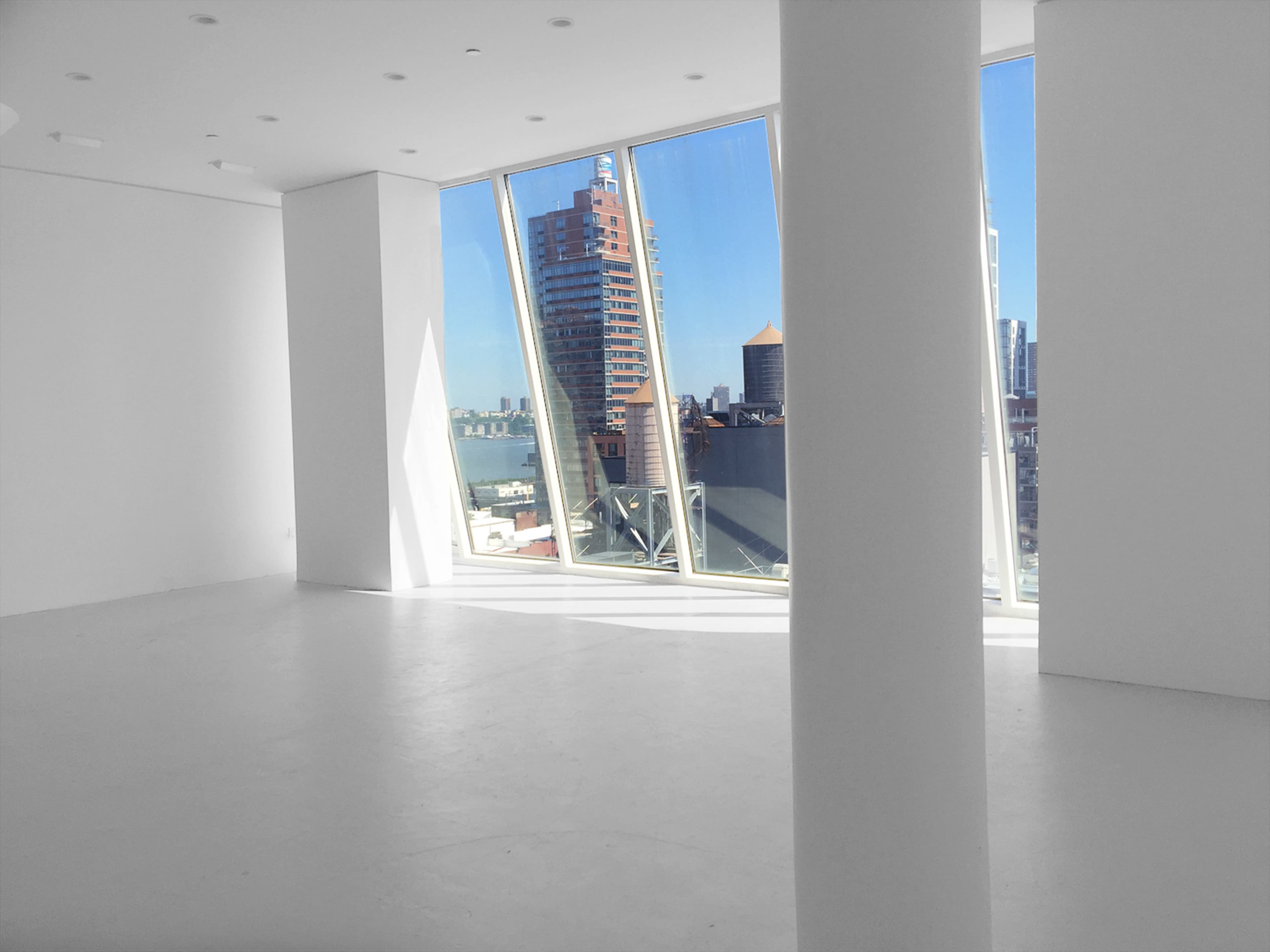 A minimalistic room with large windows providing a view of a city skyline against a clear blue sky.