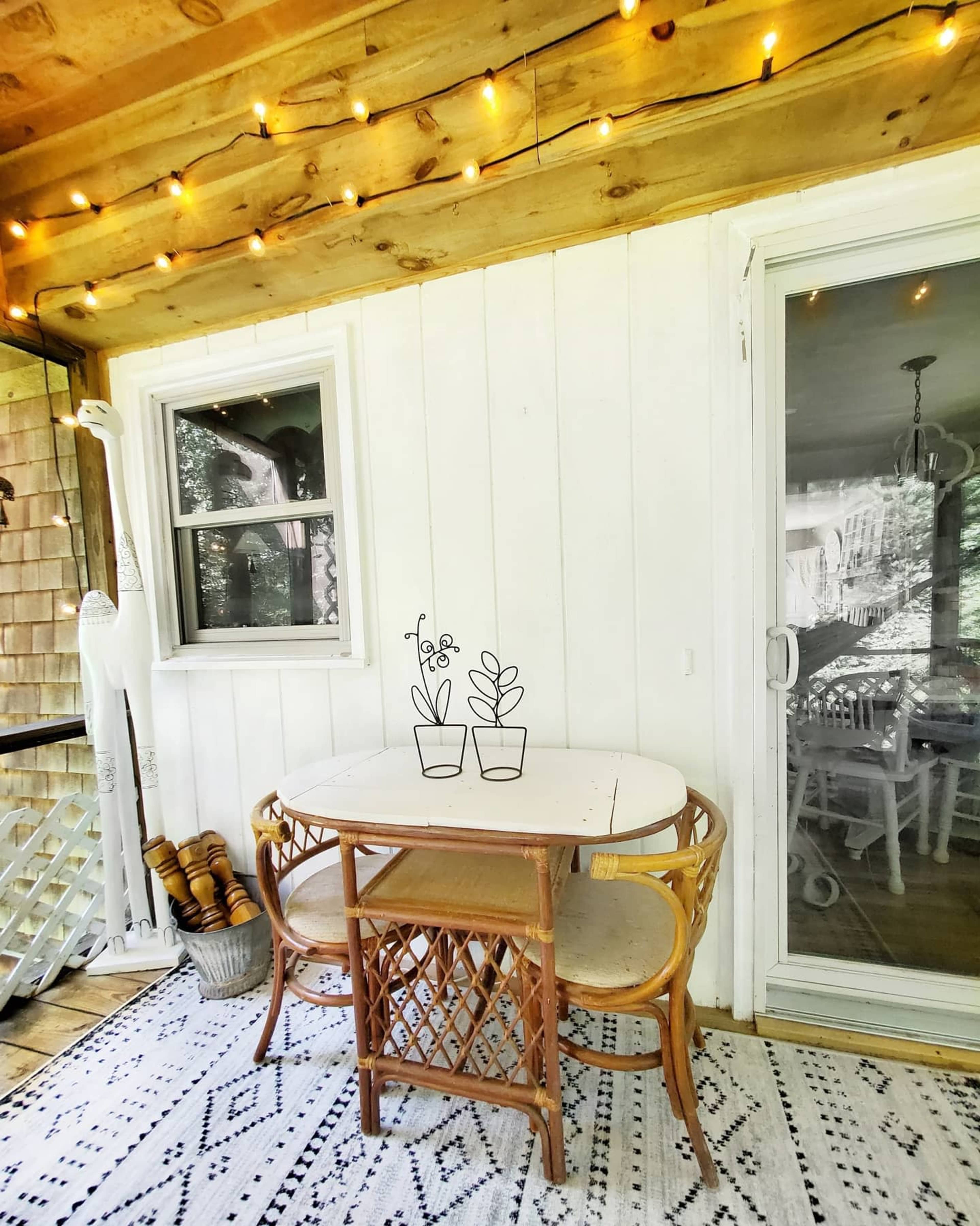 A small, decorated outdoor seating area features a round table with two chairs, surrounded by string lights and a patterned rug.