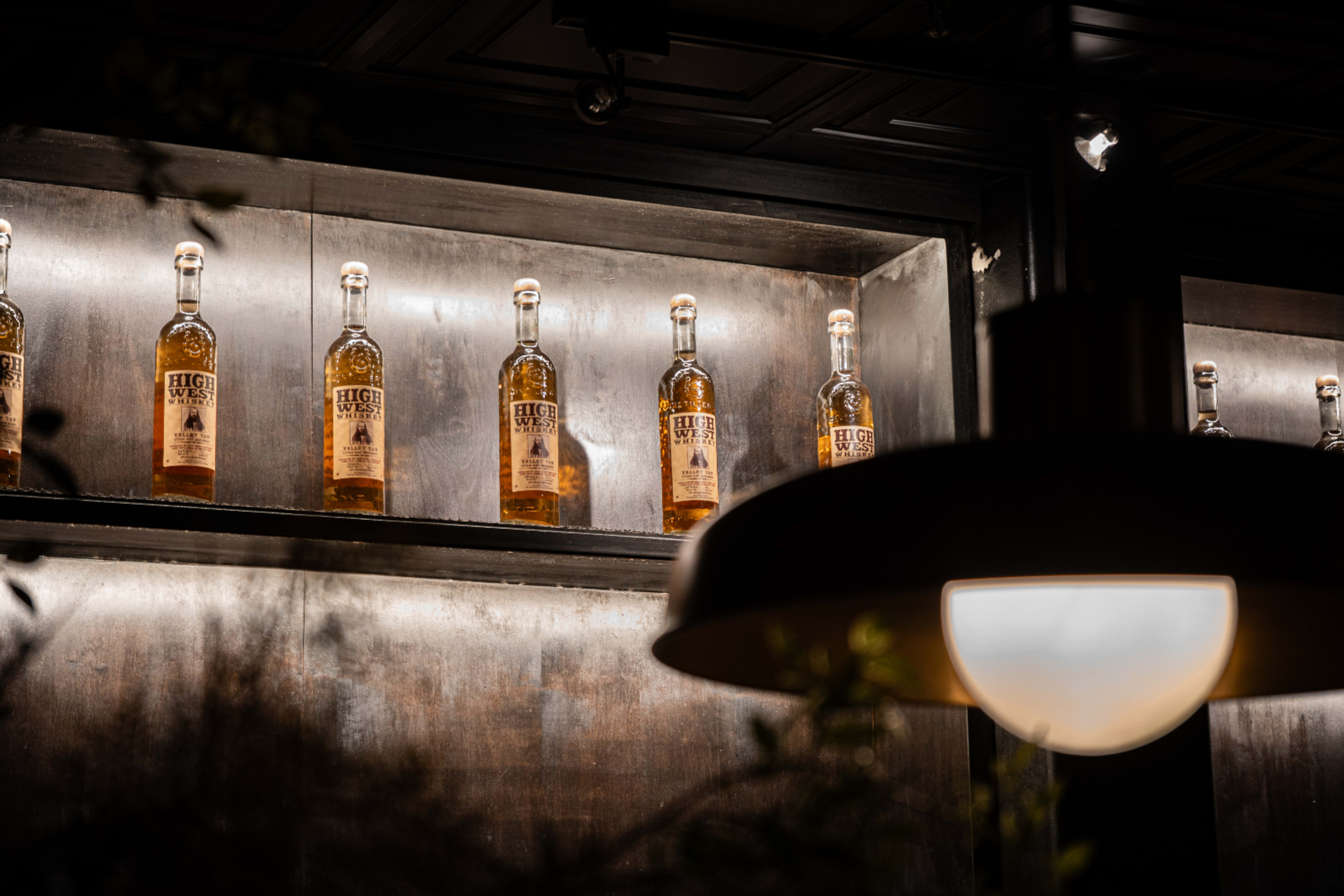 A row of bottles labeled "HUGE" is displayed on a wooden shelf with a pendant light in the foreground.