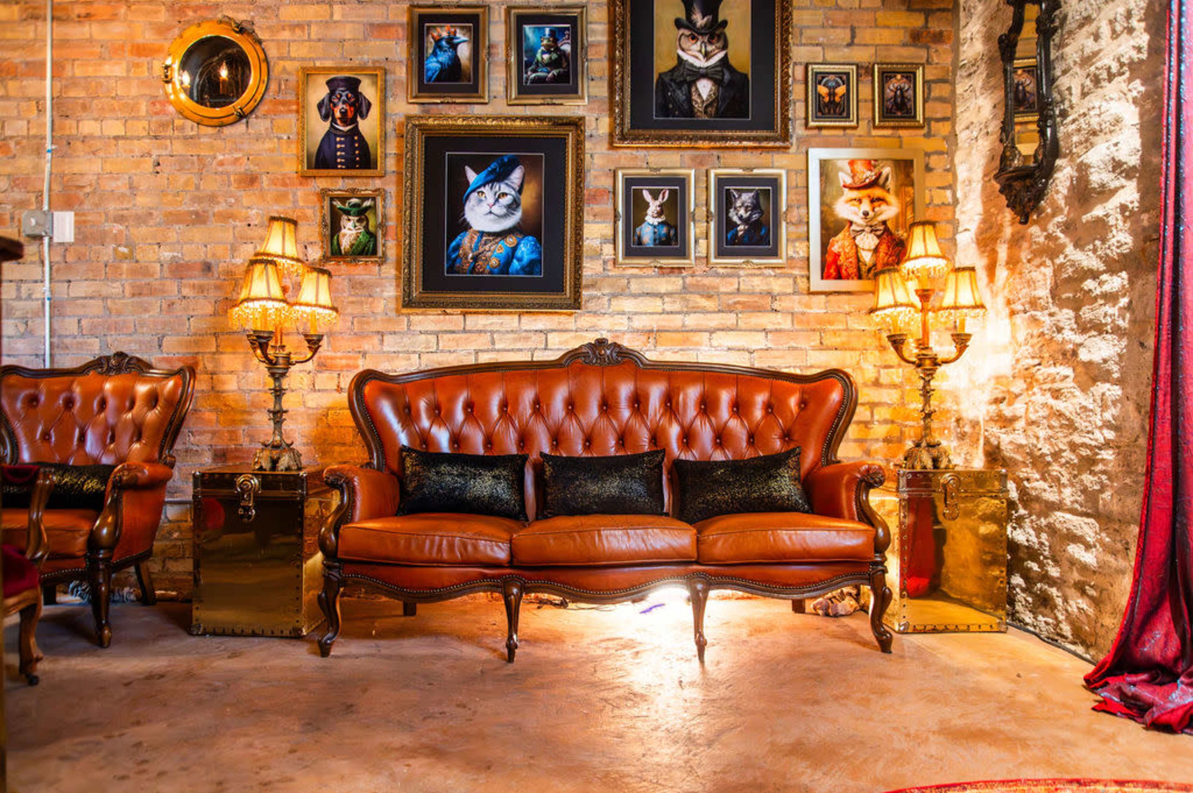 The image shows a vintage-style living room featuring a brown leather couch, ornate lamps, and a wall adorned with framed portraits of cats in various costumes.