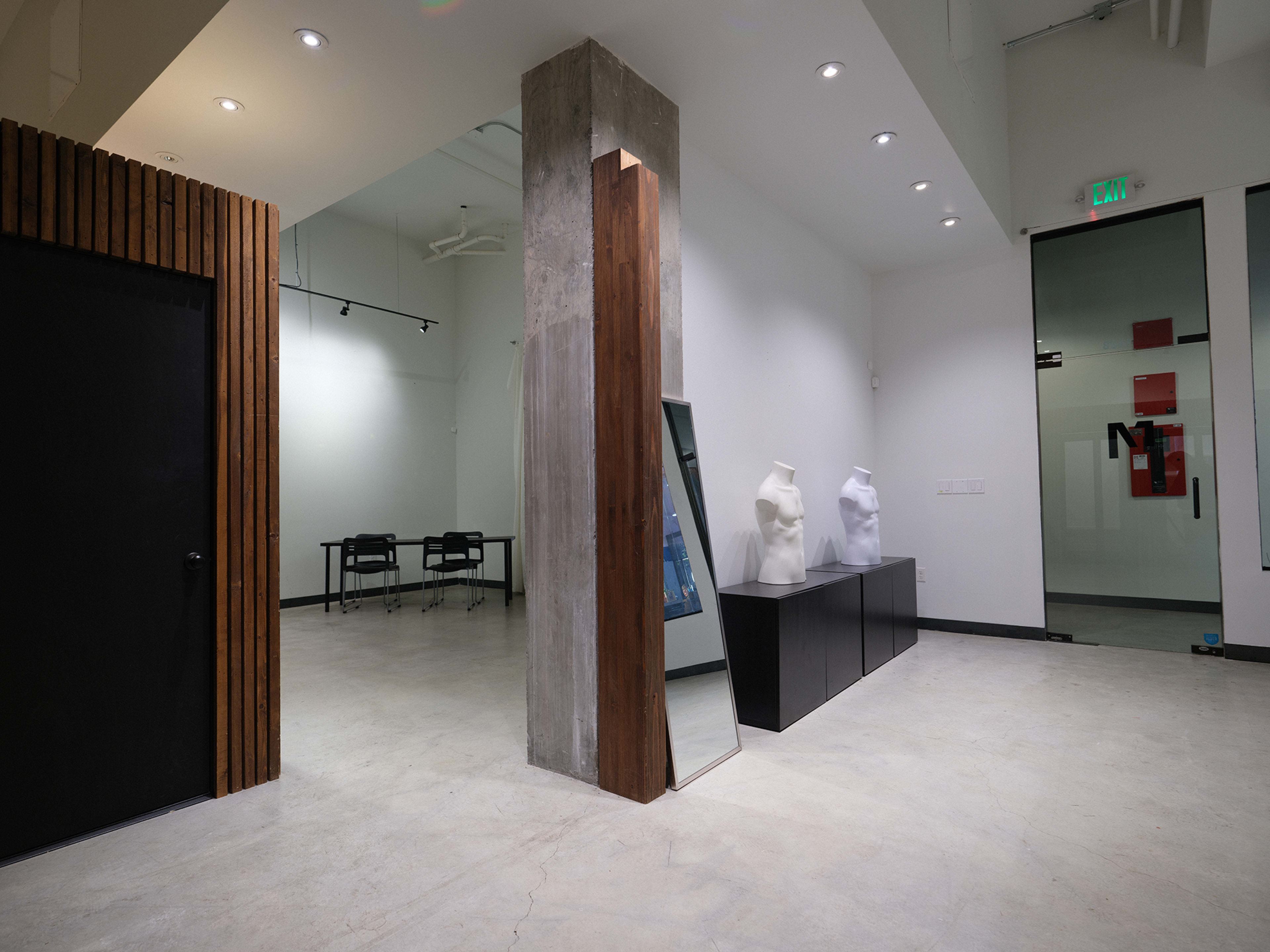 The image shows a modern interior space featuring a concrete column, black and white decor, a mirror, and two abstract sculptures on a low black display.