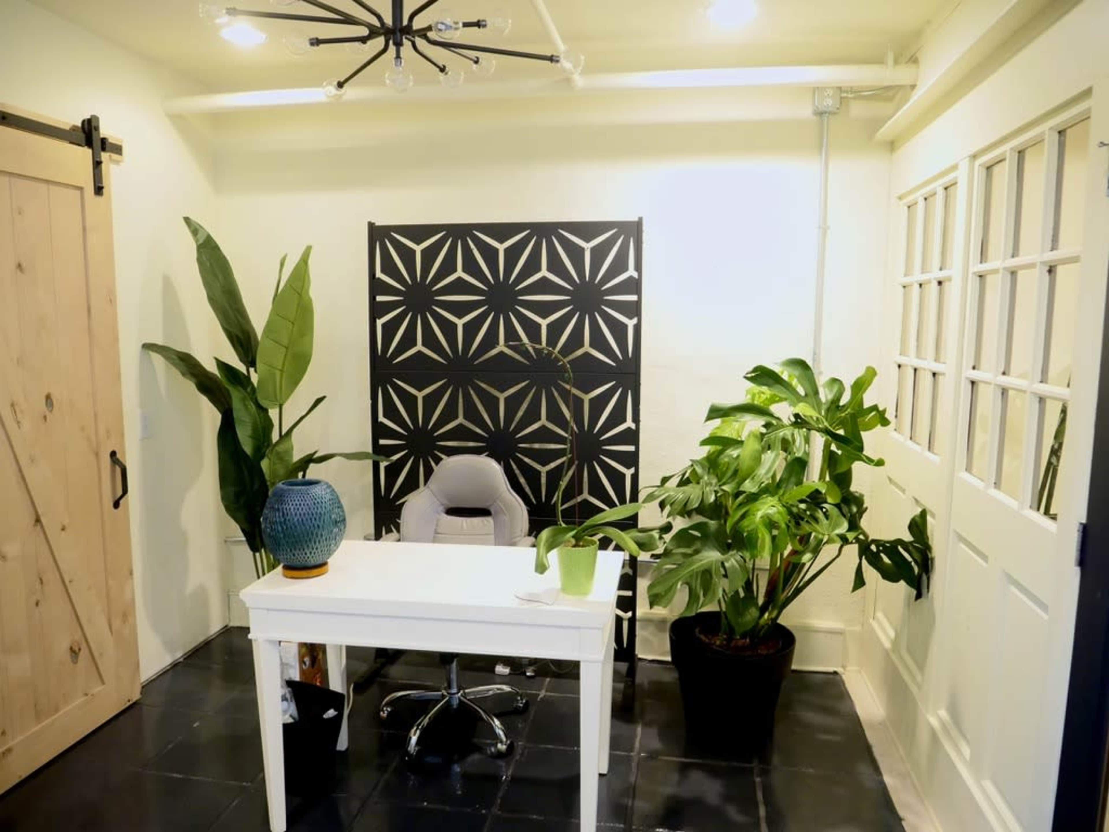 A modern office space featuring a white desk, an ergonomic chair, decorative plants, and a patterned backdrop.