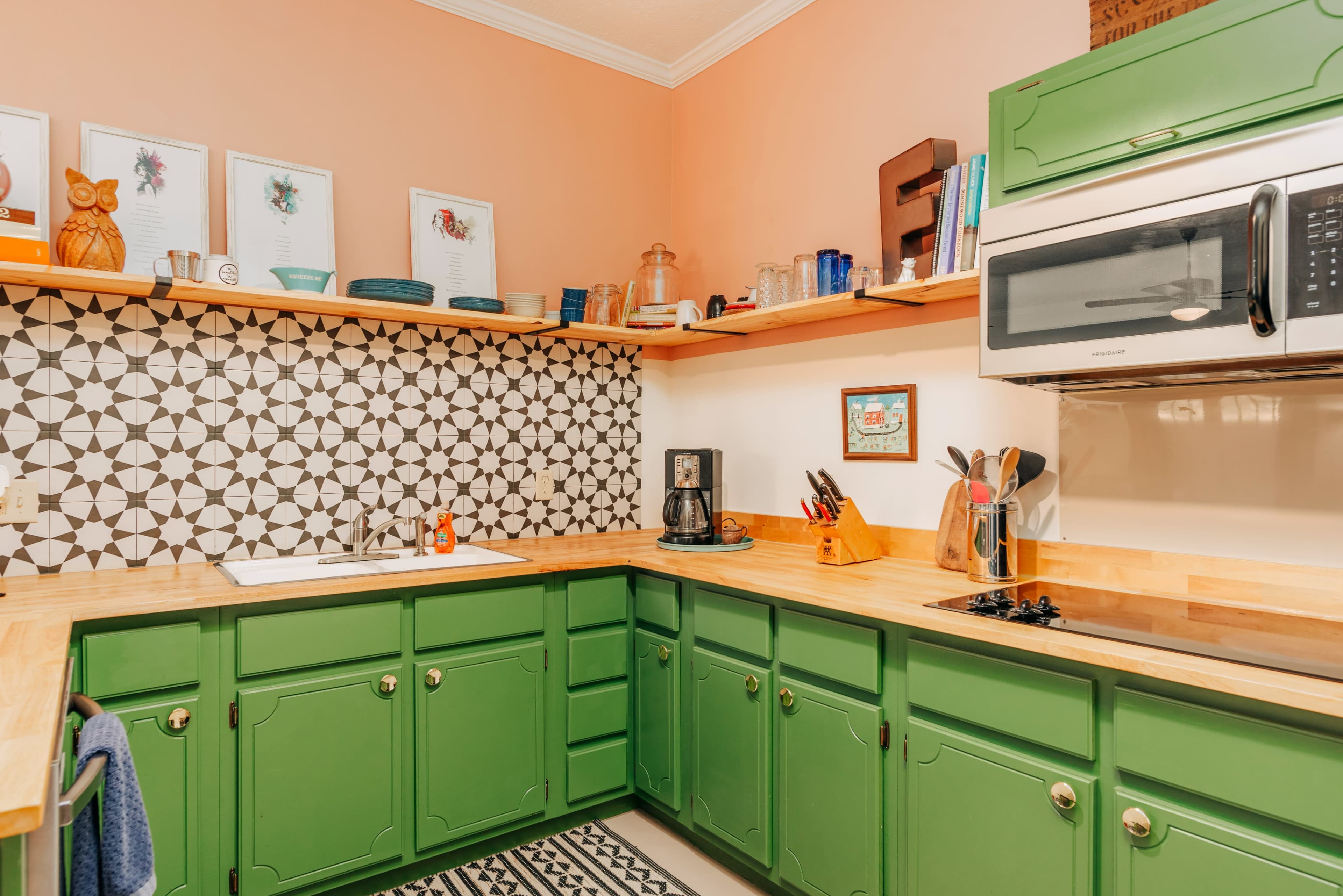 A kitchen with green cabinets, a patterned tile backsplash, and wooden countertops, featuring an array of kitchen utensils and appliances.